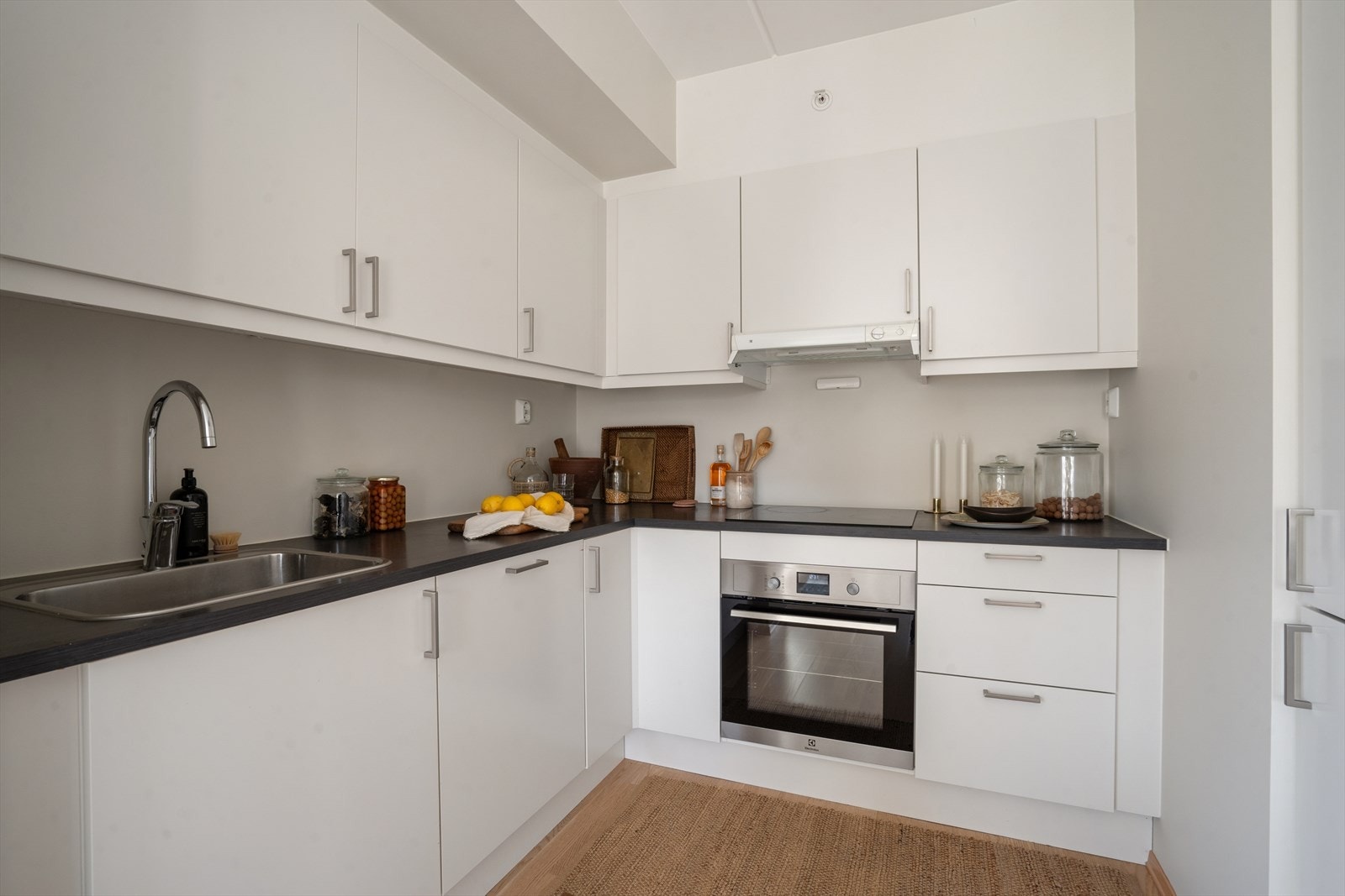 Kjøkkenet fremstår som moderne og stilrent med lyse, glatte fronter og en praktisk L-formet løsning som gir gode arbeidsflater og effektiv utnyttelse av plassen. Galleribilde