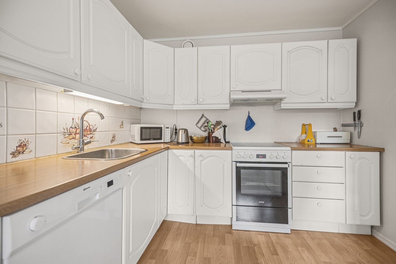 Flislagt vegg over benk gir et funksjonelt arbeidsområde, kombinert med benkebelysning under overskap. Galleribilde