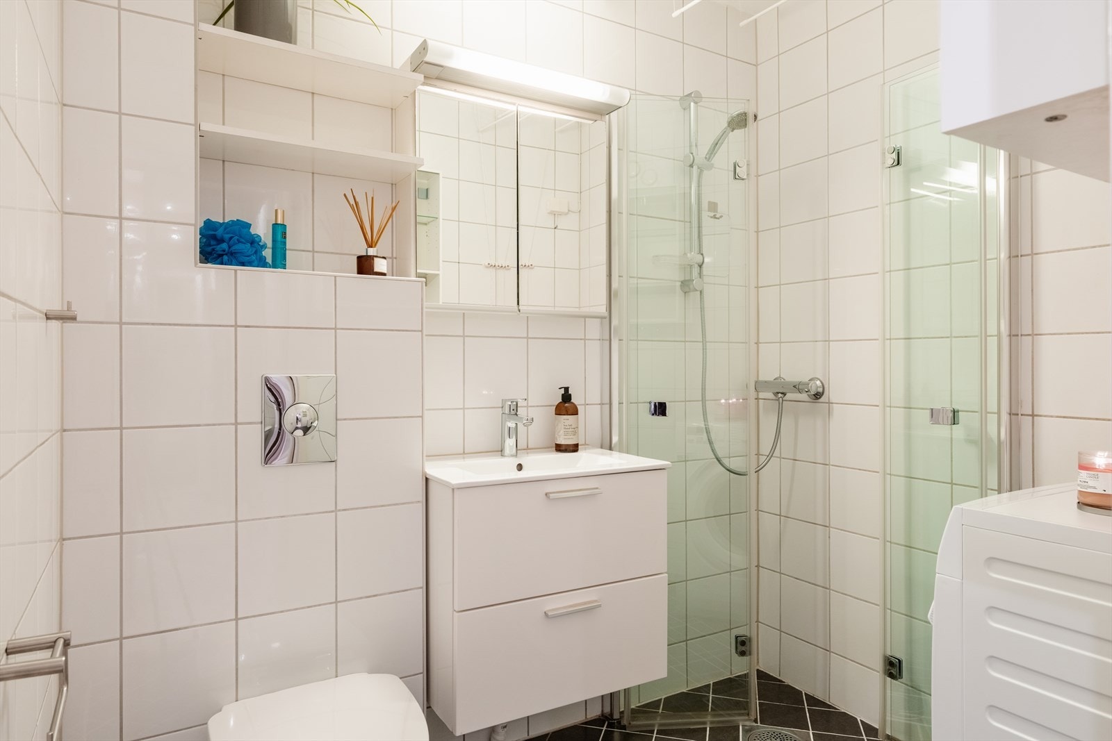 Badet har flislagte overflater, vegghengt toalett og svingbare dusjvegger i glass. Galleribilde