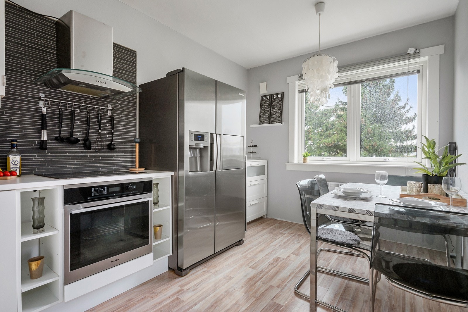 Kjøkkeninnredning med hvite, slette fronter og integrert komfyr, platetopp og oppvaskmaskin. Laminert benkeplate med lys under overskap. Galleribilde