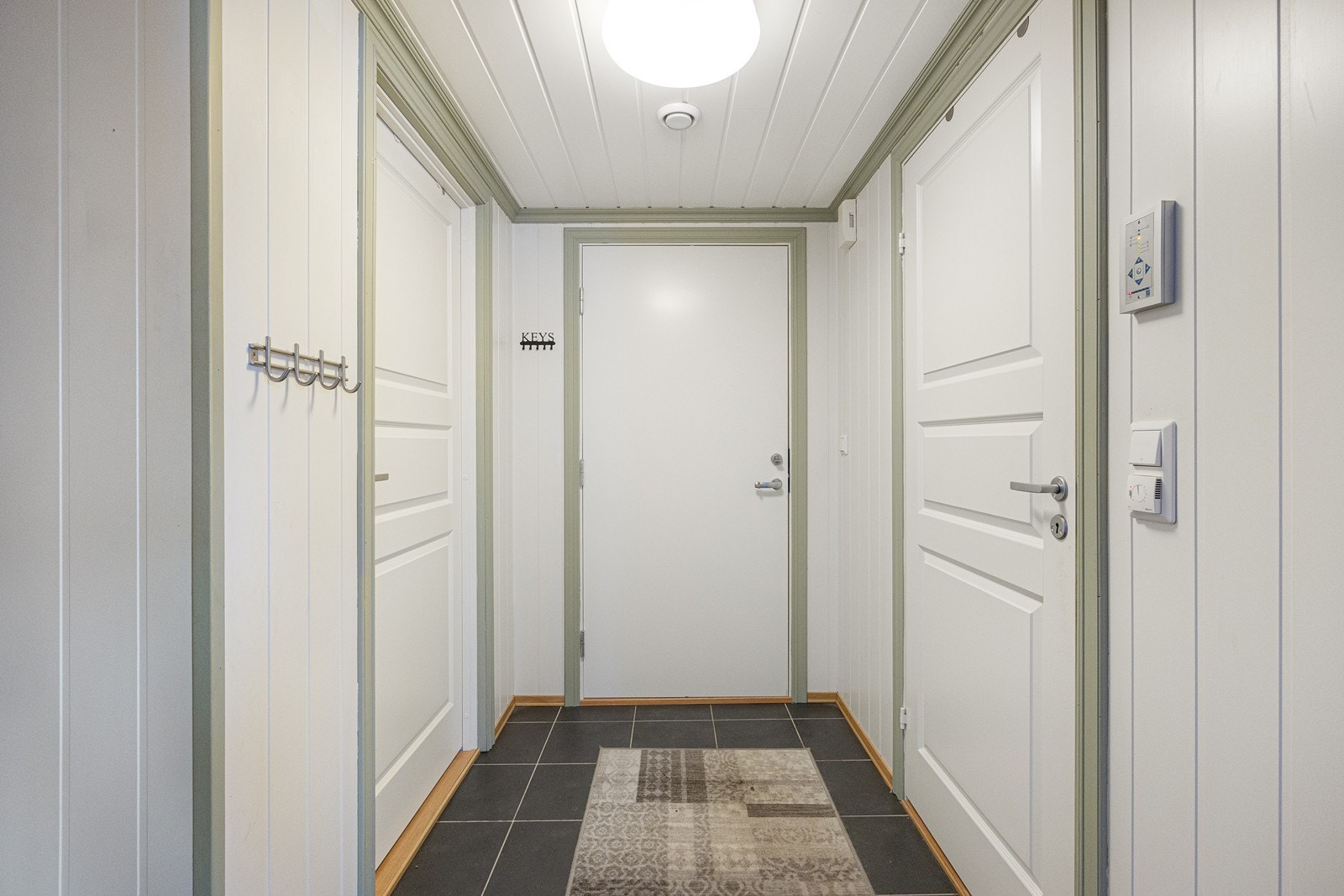 I entreen blir man ønsket velkommen i en fin entré med hvitmalt panel på veggene og koksgrå fliser på gulvet. Galleribilde