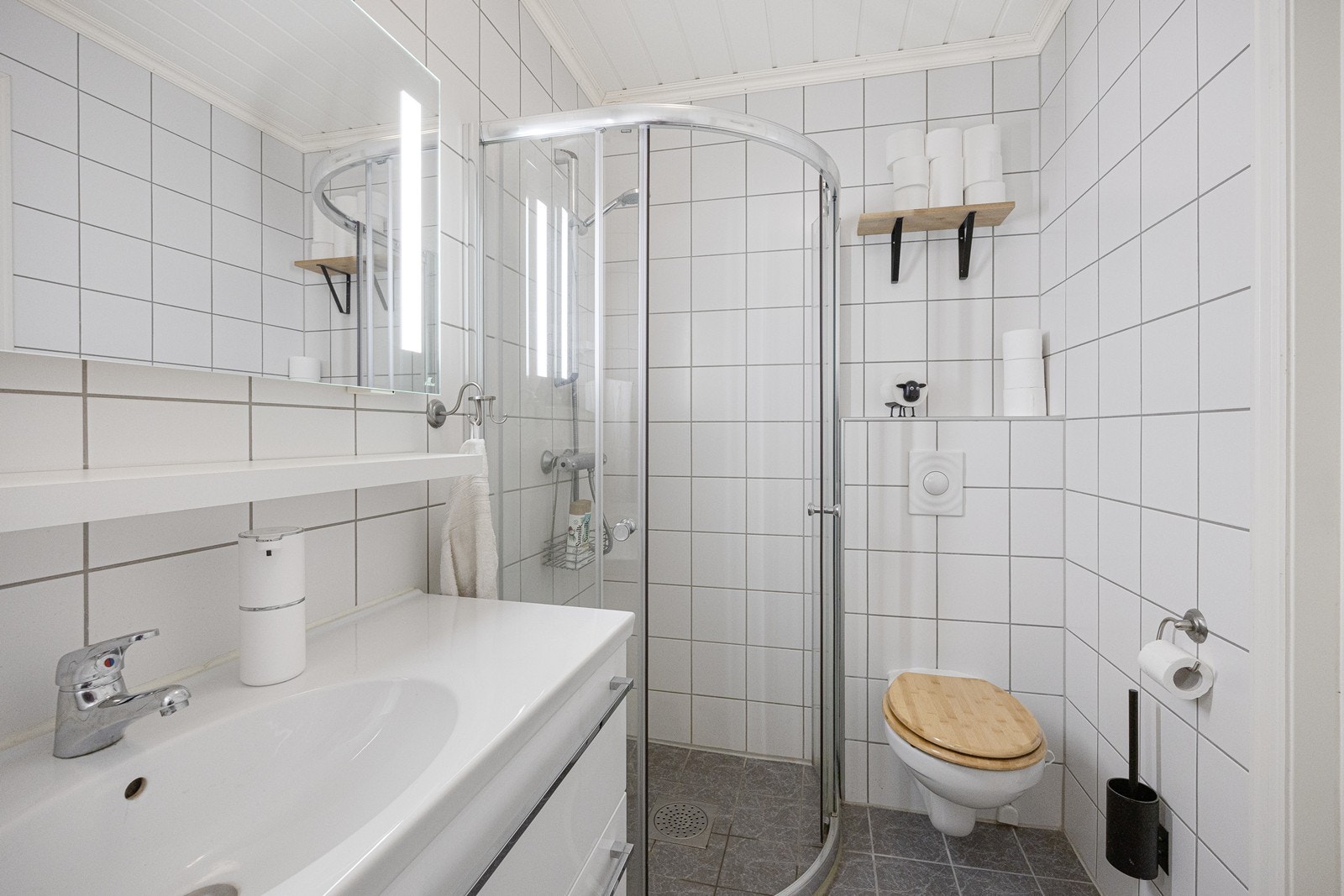 Baderomsinnredningen har hvite fronter og består av en heldekkende servant på en skuffeseksjon og et stort speil med integrert belysning. Galleribilde