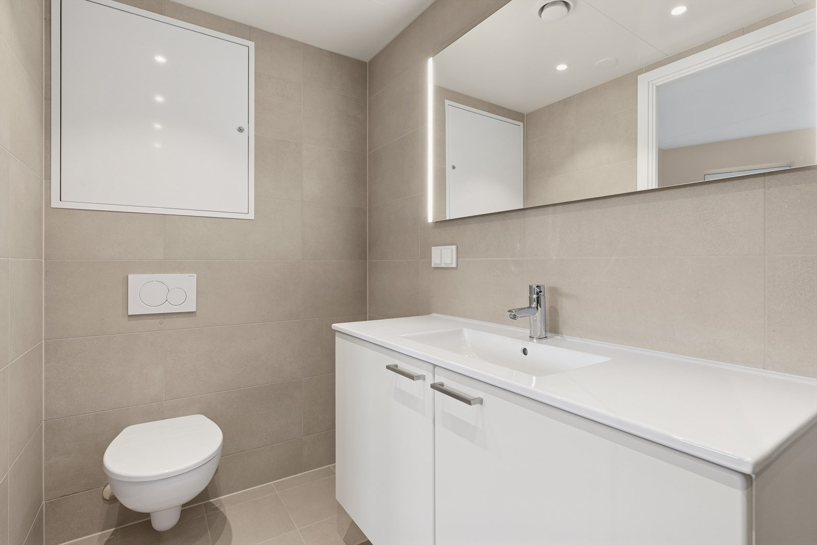 Rommet er utstyrt med dusjnisje med skjermvegg og dør av glass, vegghengt klosett, hel nedfelt servant og baderomsinnredning med servantskap og speil med integrert belysning. Galleribilde