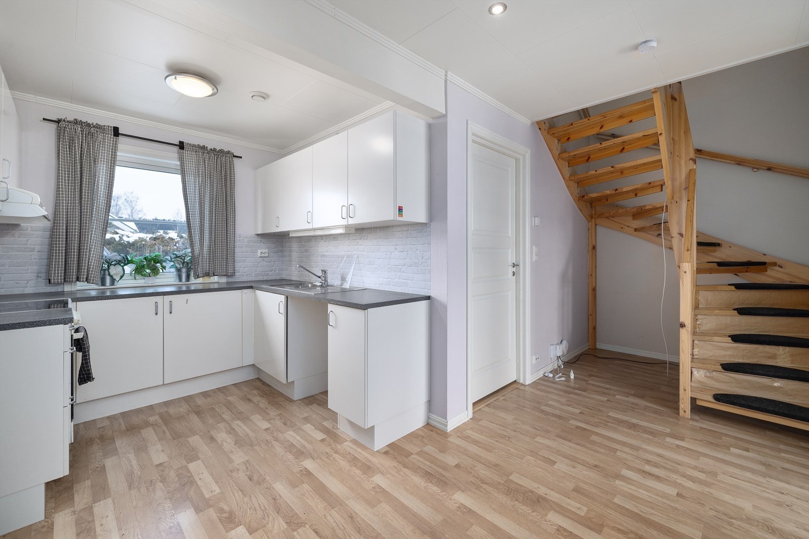 Kjøkkenet har en lys innredning med glatte fronter. Den lakkerte tretrappen leder opp til andre etasje. Galleribilde