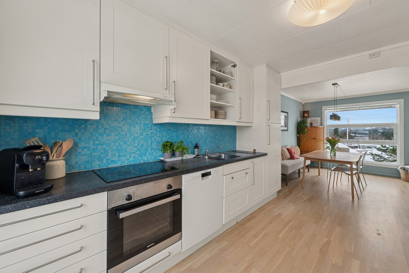 Det er "takhøy" kjøkkeninnredning med profilerte folierte fronter med 1 speil, laminat benkeplate, mosaikkfliser over benken, ventilator og underlimt stål benkebeslag. Galleribilde