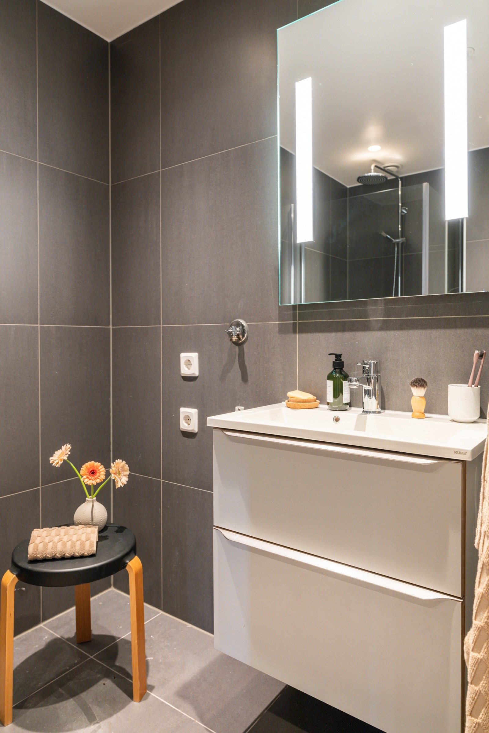 Moderne baderomsinnredning med skuffer og heldekkende servant, speil med integrert belysning over. Galleribilde