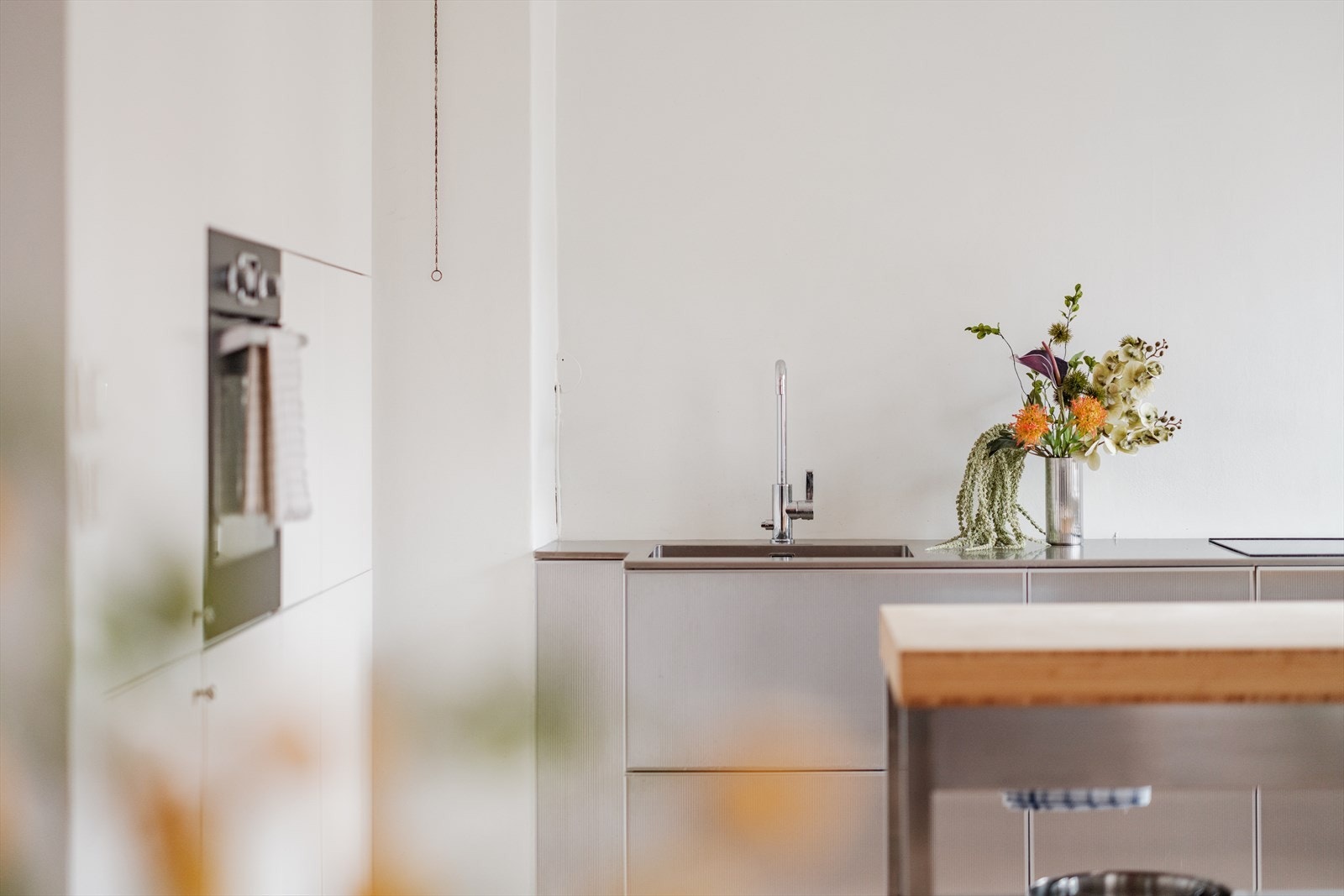 Takhøyden og den åpne løsningen mot stuen gir rommet en luftig og sosial atmosfære, samtidig som kjøkkenet er diskret plassert i en egen, koselig nisje perfekt for både matlaging og samtaler over kaffekoppen. Galleribilde