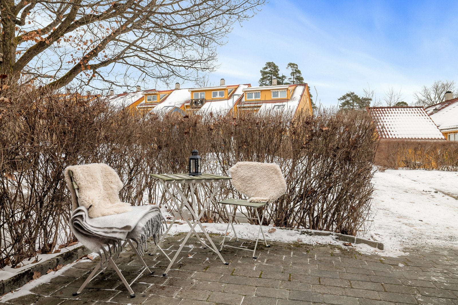 Stensatt uteplass ved inngangspartiet som er skjermet av hekk. Galleribilde