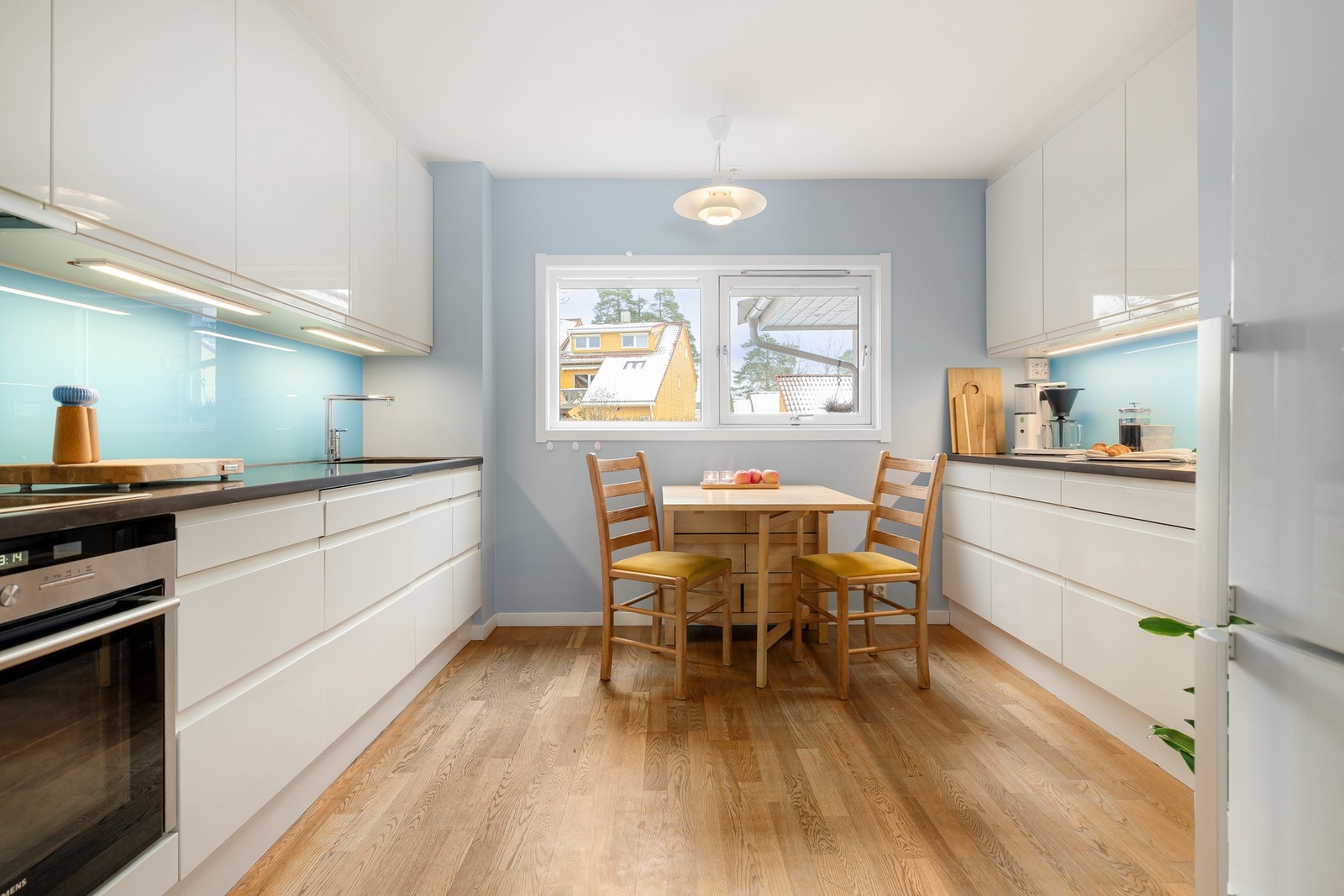 Lyst og stilrent HTH-kjøkken fra 2010 med glatte, hvite fronter. Benkeplaten består av komposittstein med underlimt kum i rustfritt stål. Galleribilde