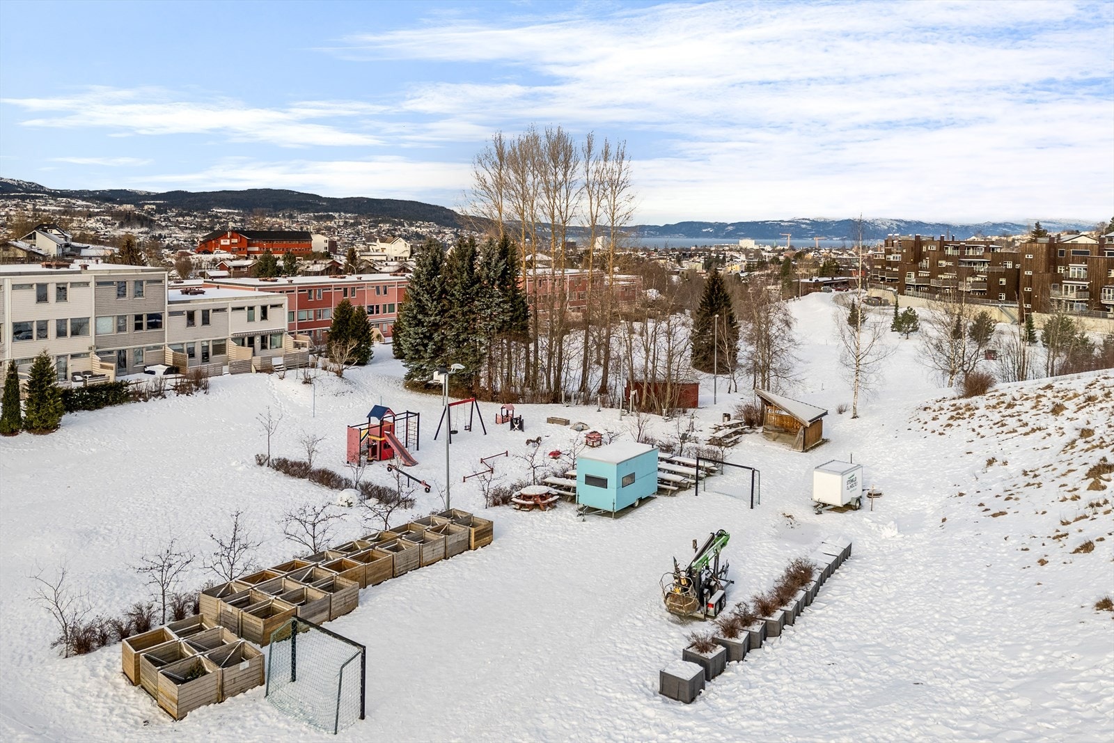 Dronebilde med boligen til venstre og dalen med parseller hvor du kan dyrke grønnsaker samt flott lekeplass med gapahuk. Galleribilde