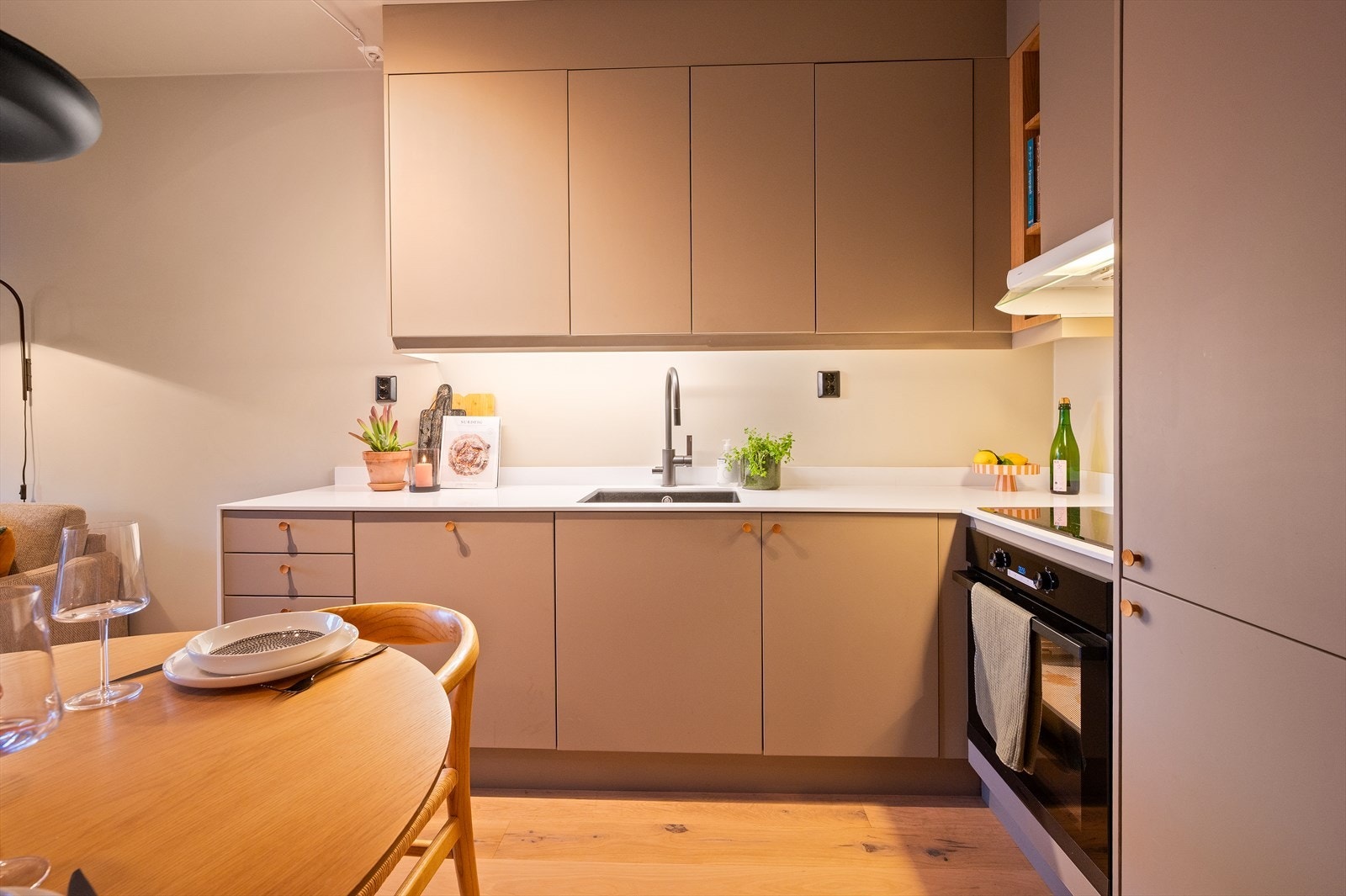 Moderne kjøkkeninnredning fra Sigdal med glatte, beige fronter og Corian benkeplate med integrert oppvaskkum og ettgreps, svingbart blandebatteri. Kjøkkenet har rikelig med skap- og benkeplass, samt integrert kjøl/frys og oppvaskmaskin. Galleribilde