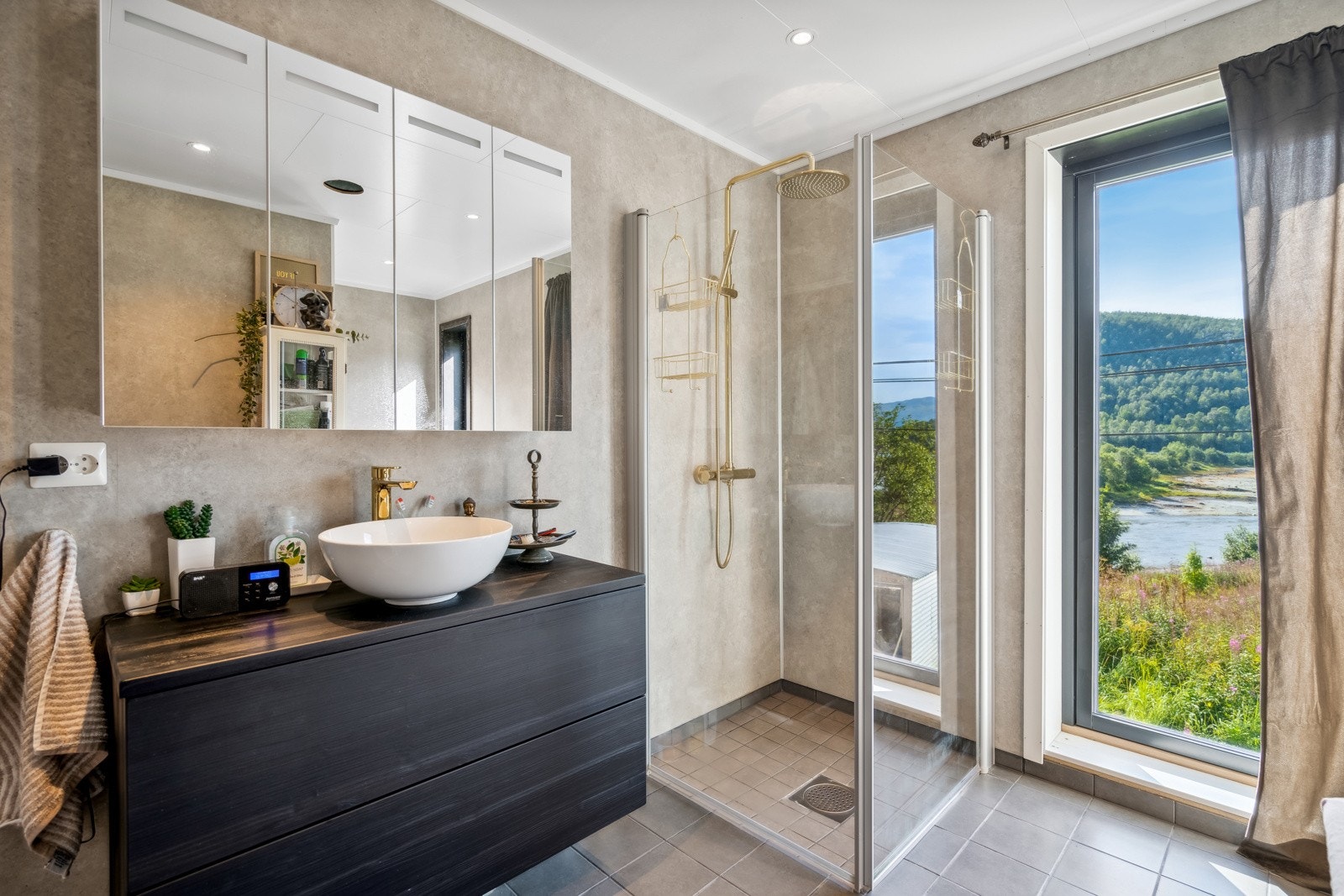 Flislagt bad med dusj, vegghengt servant og oppbevaring i baderomsmøblement. Galleribilde