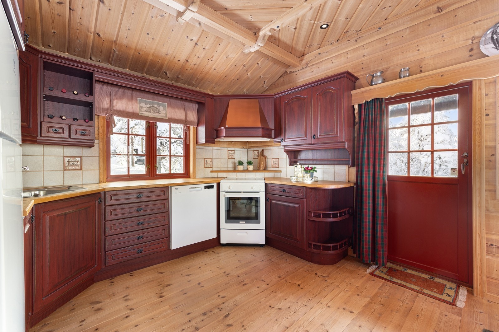 Praktisk kjøkken utstyrt med kjøle- og fryseskap, oppvaskmaskin og komfyr. Utgang direkte ut til den overbygde sydvendte terrassen fra kjøkkenet Galleribilde