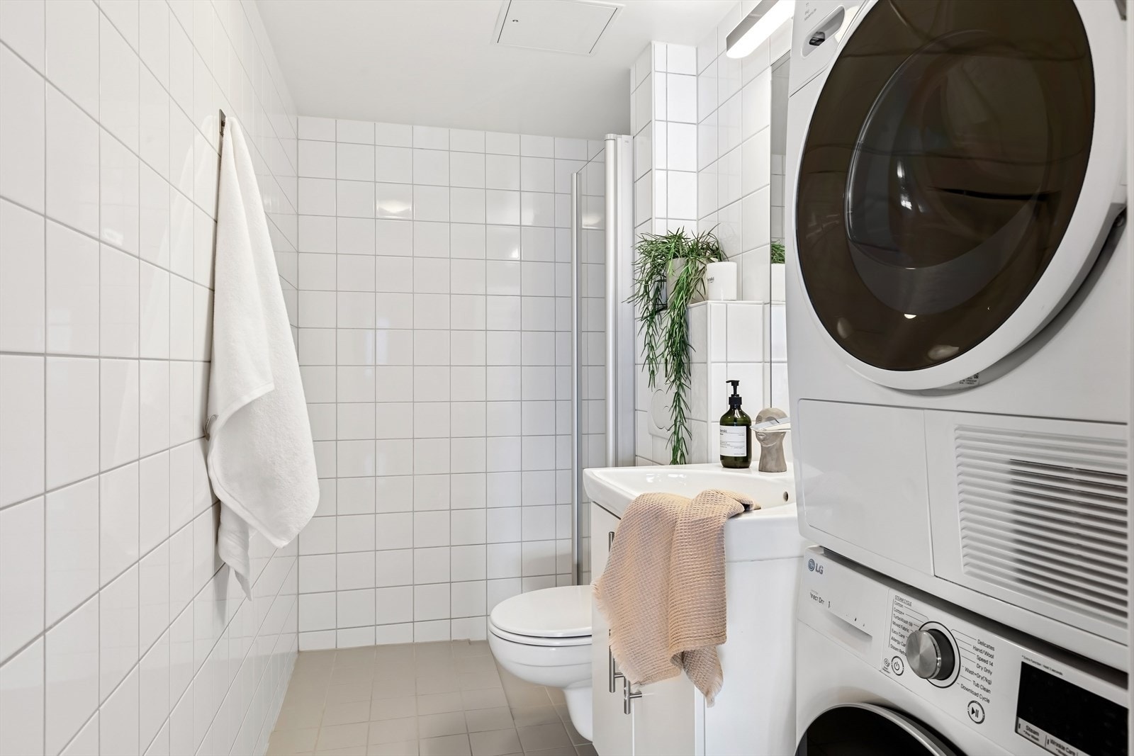 Flislagt bad med dusj, servantinnredning og opplegg for vaskemaskin. Galleribilde