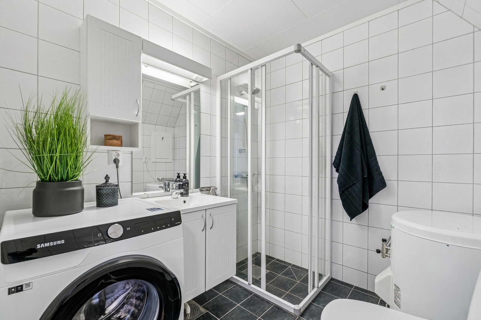 Leiligheten har et tidløst bad med sort gulv og en hvit utførelse på vegger og himling. Galleribilde