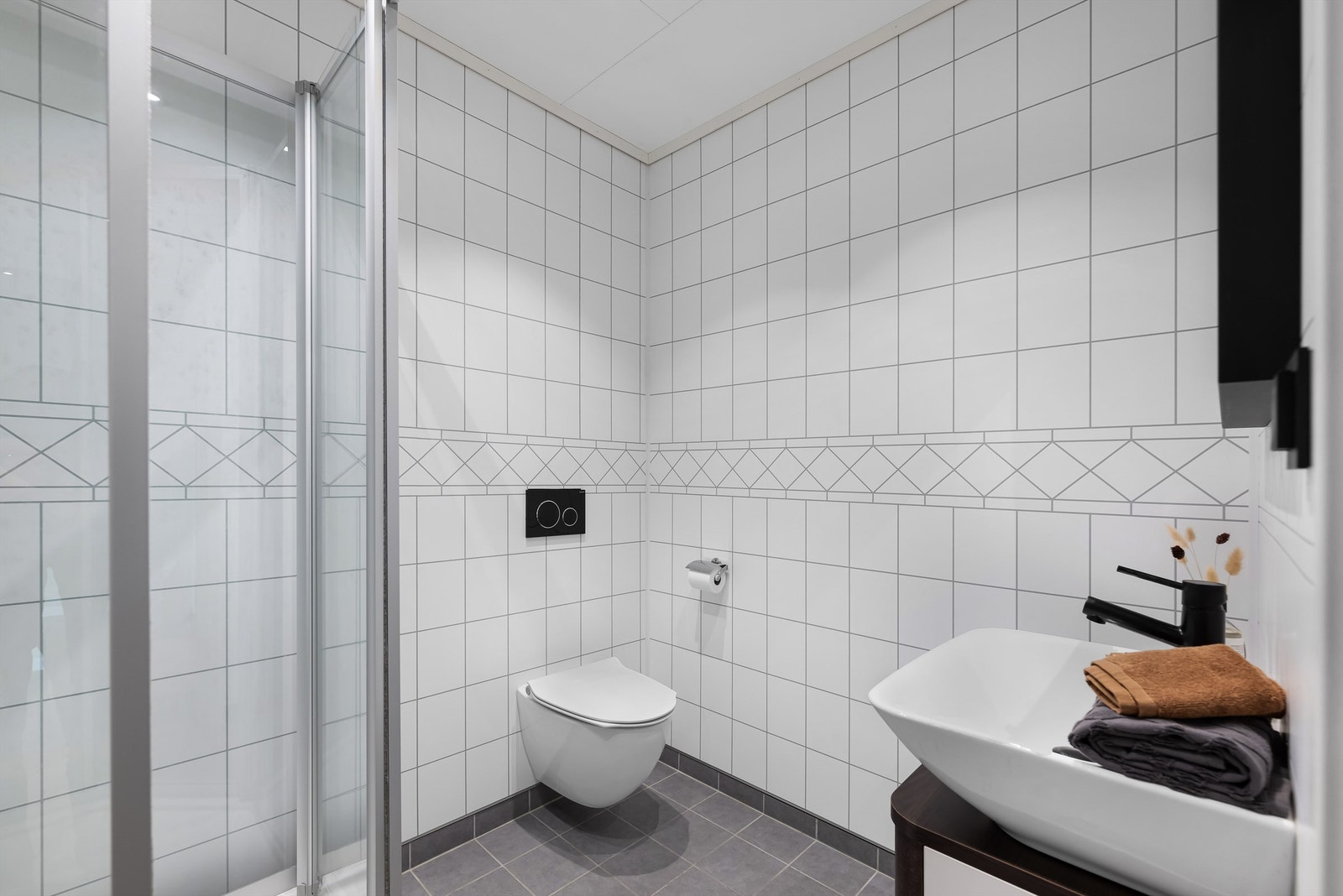 Moderne bad med fliser på gulv og plater på vegger, innredet med vegghengt wc, dusj og servant med baderomsinnredning Galleribilde