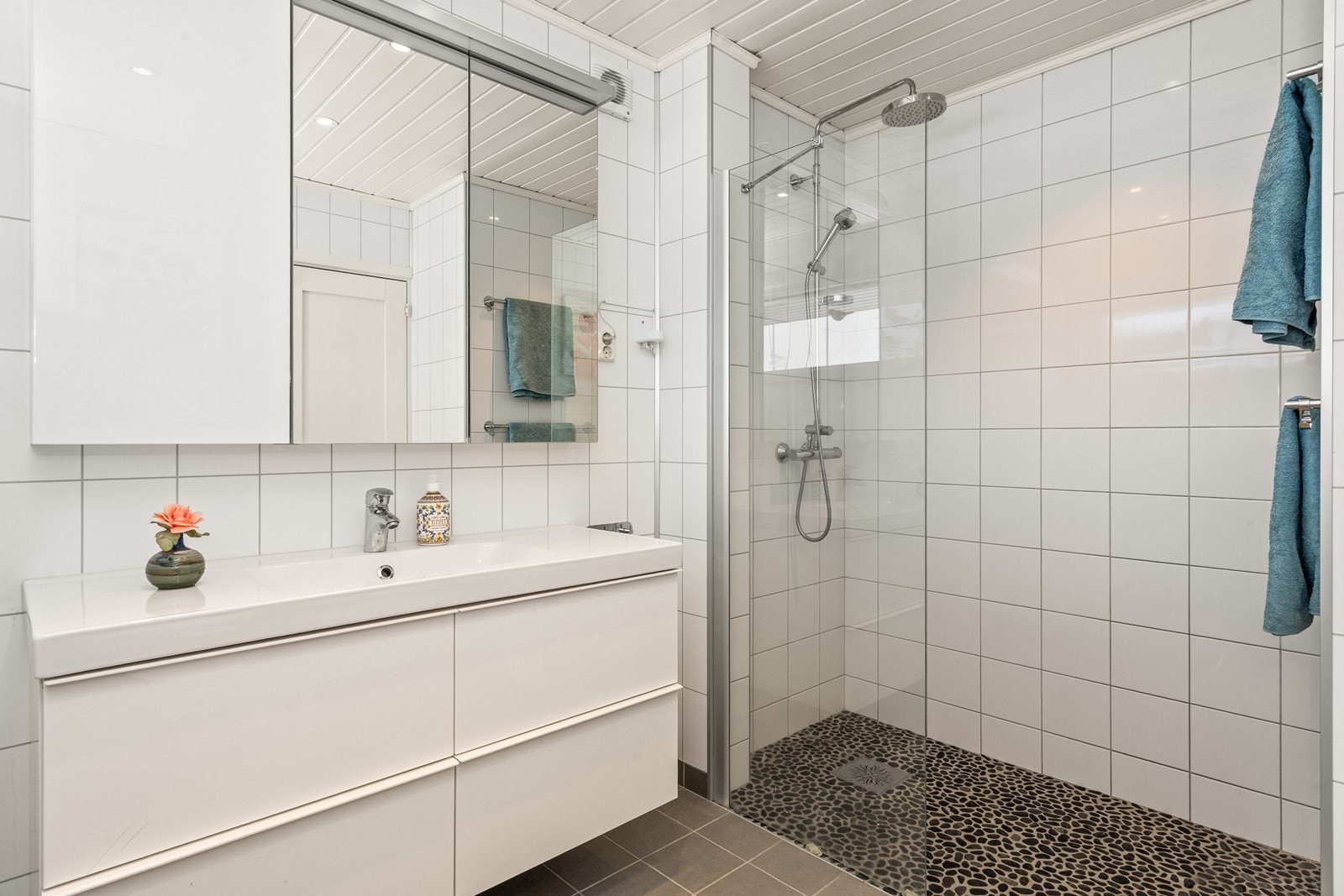 Badet har servantinnredning, speilskap med integrert belysning, en nedsenket dusjnisje med glassdør og vegghengt toalett Galleribilde