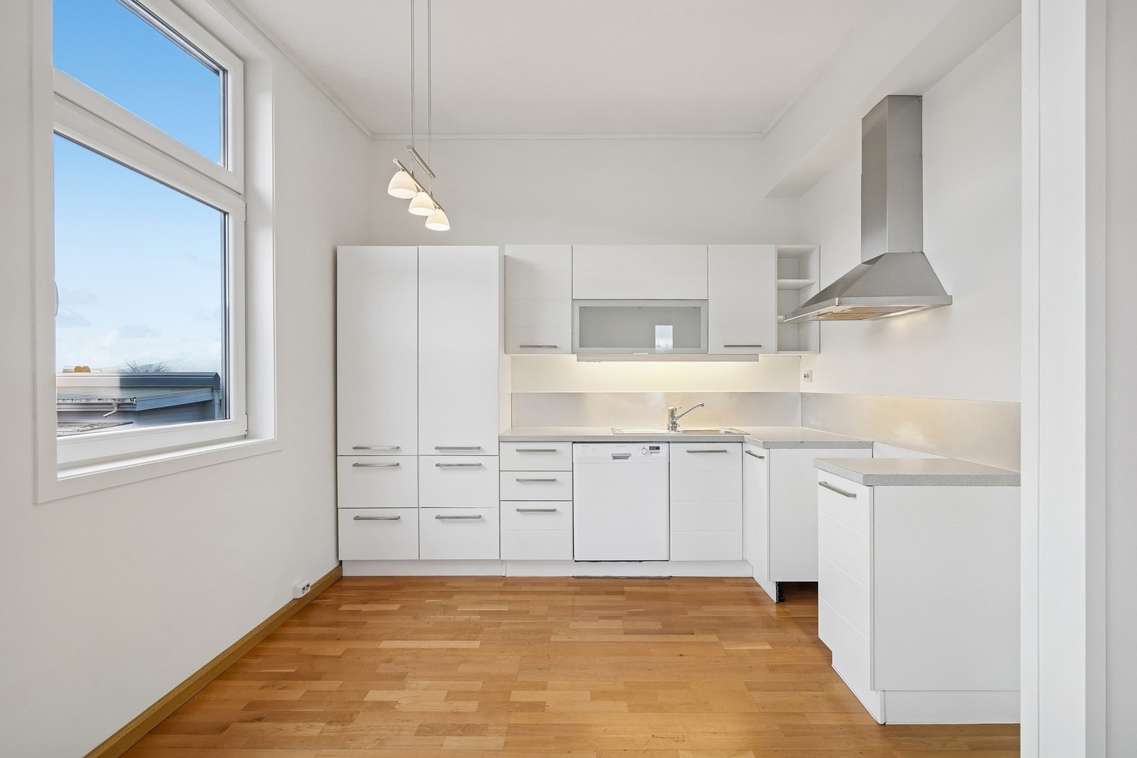 Fin kjøkkeninnredning med hvite fronter og laminat benkeplate. Det er plass til mindre sittegruppe ved vindu. Galleribilde