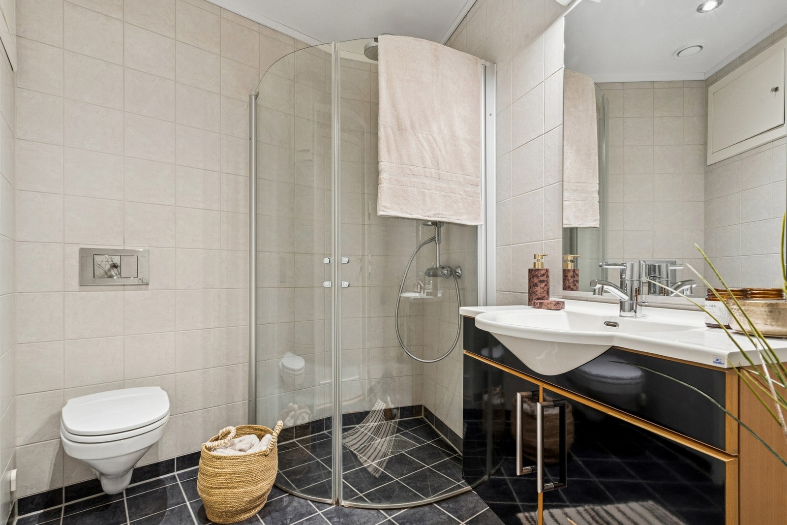 Pent, flislagt baderom utstyrt med servantinnredning, toalett, dusj og opplegg for vaskemaskin. Galleribilde