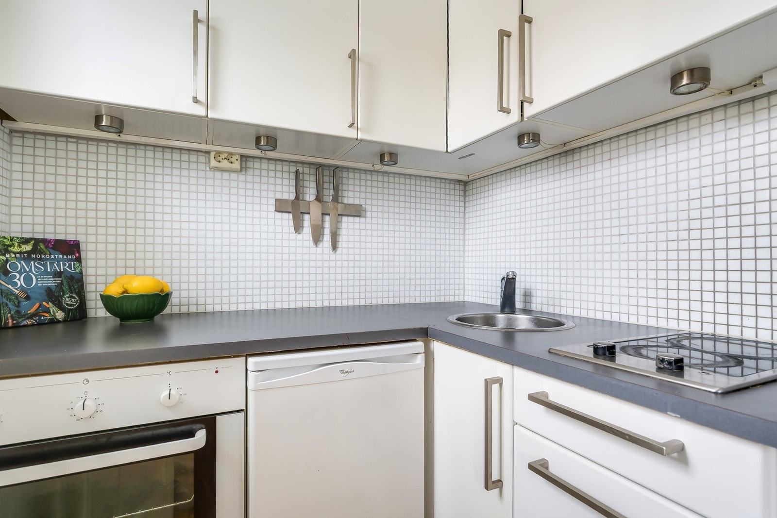 Kjøkken med glatte fronter, laminat benkeplate, flislagt vegg og integrerte hvitevarer med platetopp og komfyr Galleribilde