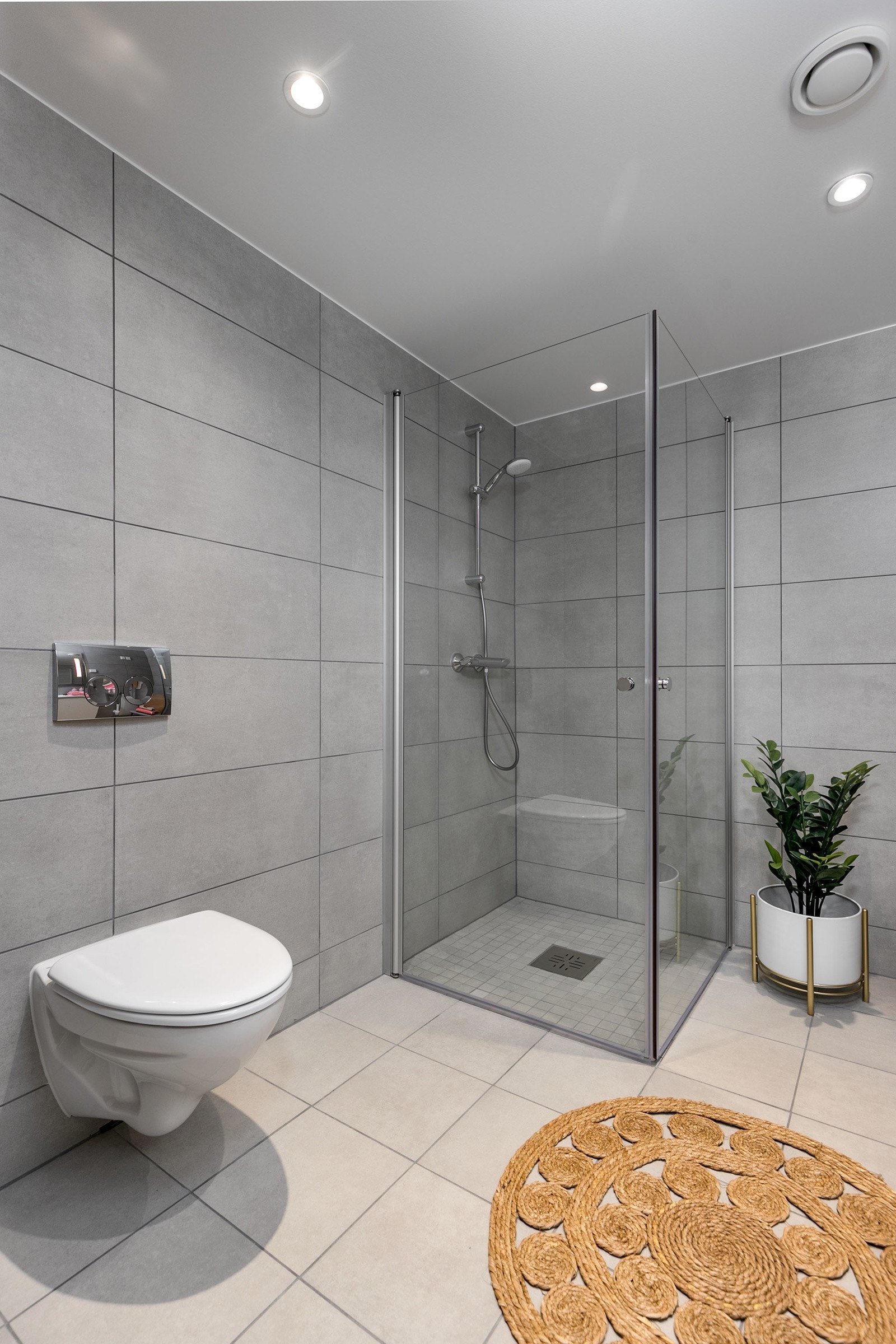 Delikat flislagt bad med vegghengt toalett, dusjsone med innfellbare dører samt servant med skapinnredning. Bilde fra L207 Galleribilde