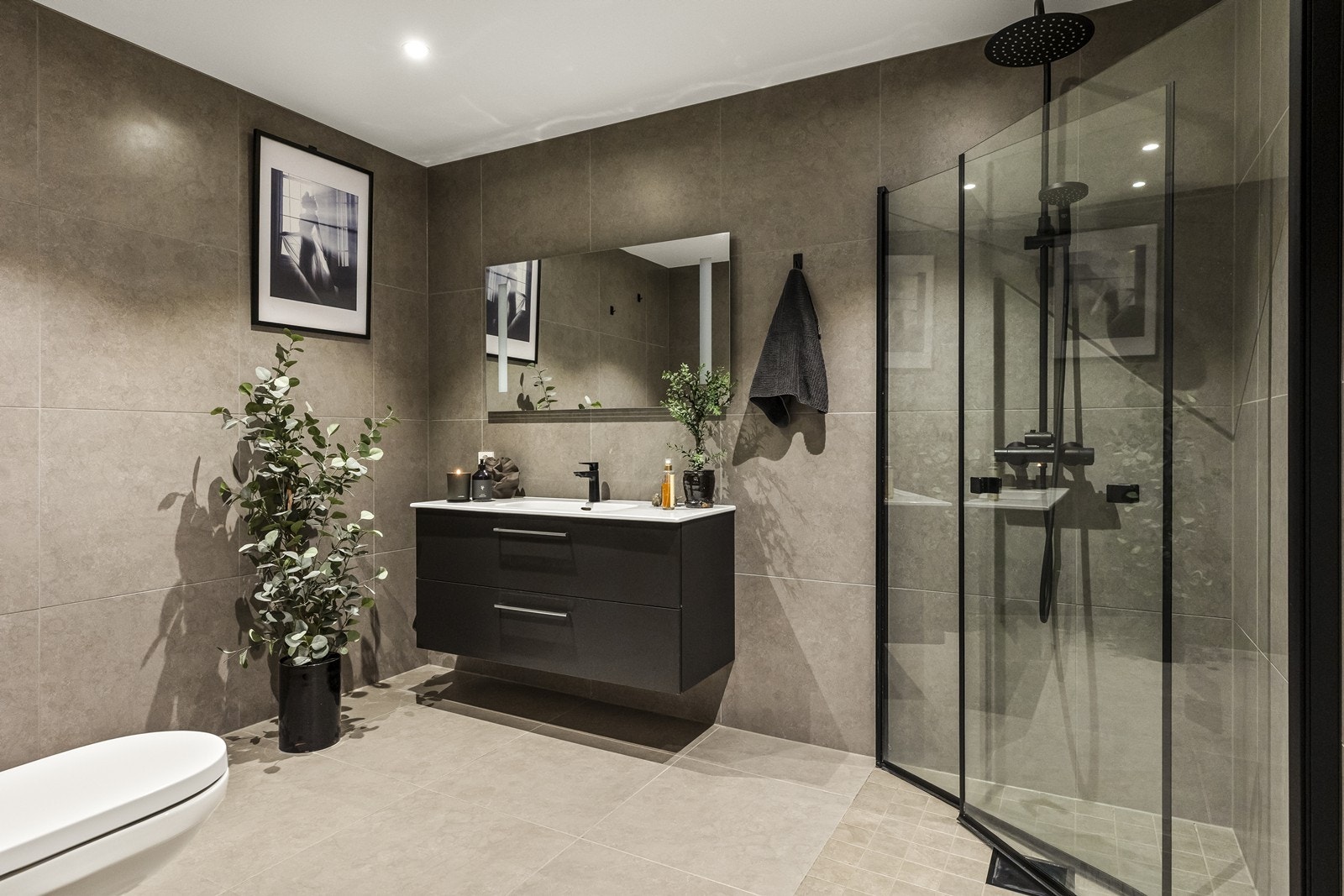 Lekkert bad/wc med 60 x 60 fliser med underliggende varmekabler på gulv og 60 x 60 fliser på vegger. Vegghengt toalett. Dusjhjørne med dusjvegger på 100 cm x 100 cm. LED downlights i tak Galleribilde