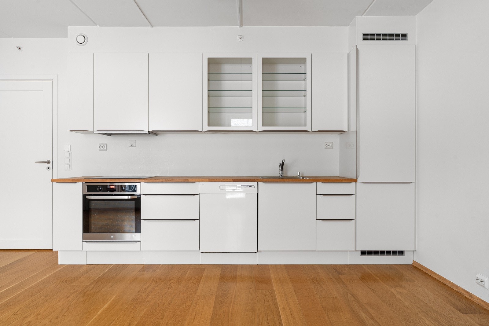 Pent og moderne kjøkken  med glatte fronter. Benkeplaten er av heltre. Det er kjøl/fryseskap, oppvaskmaskin, platetopp og stekeovn.