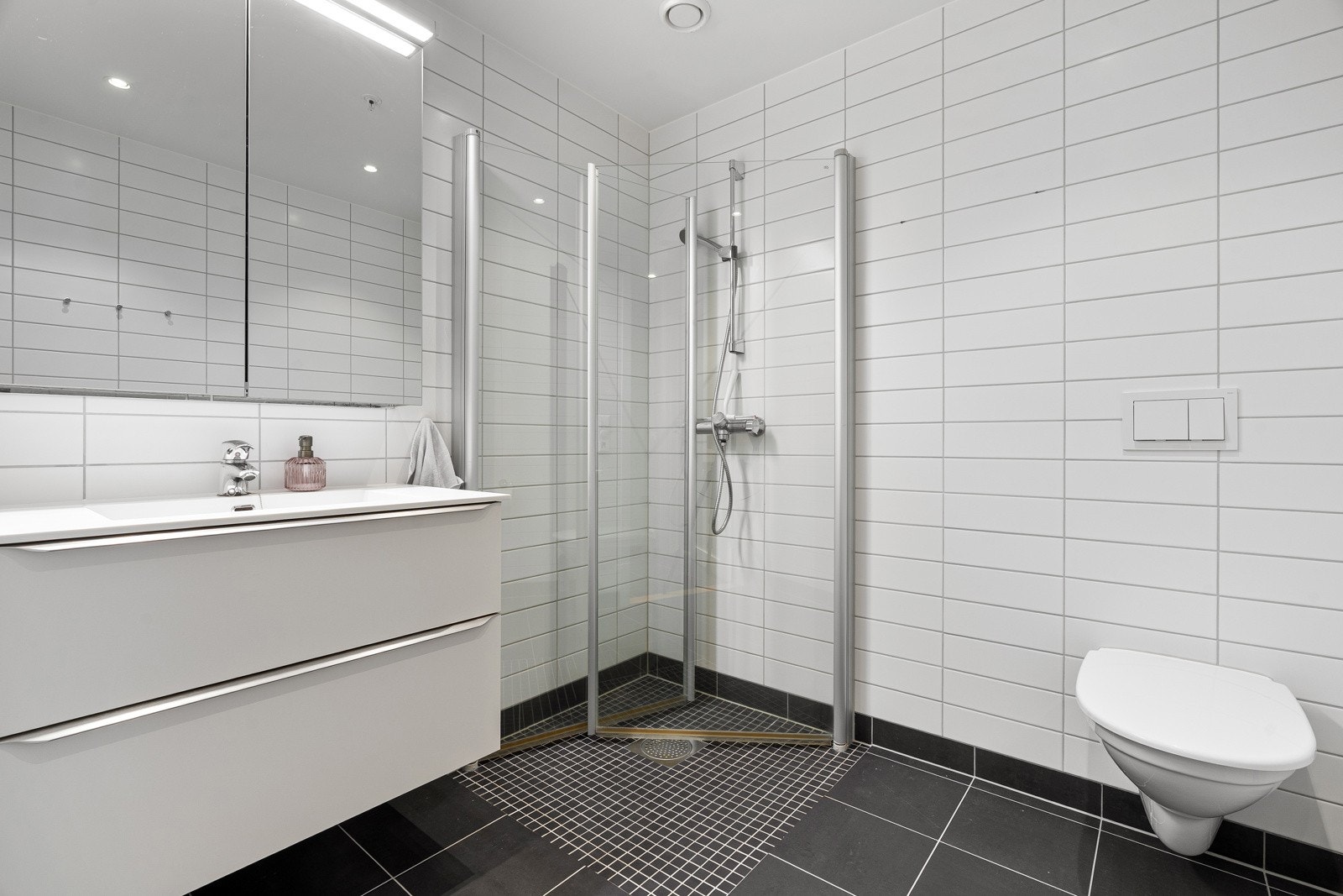 Delikat flislagt baderom med dusjhjørne, moderne innreding med skuffer og speilskap.