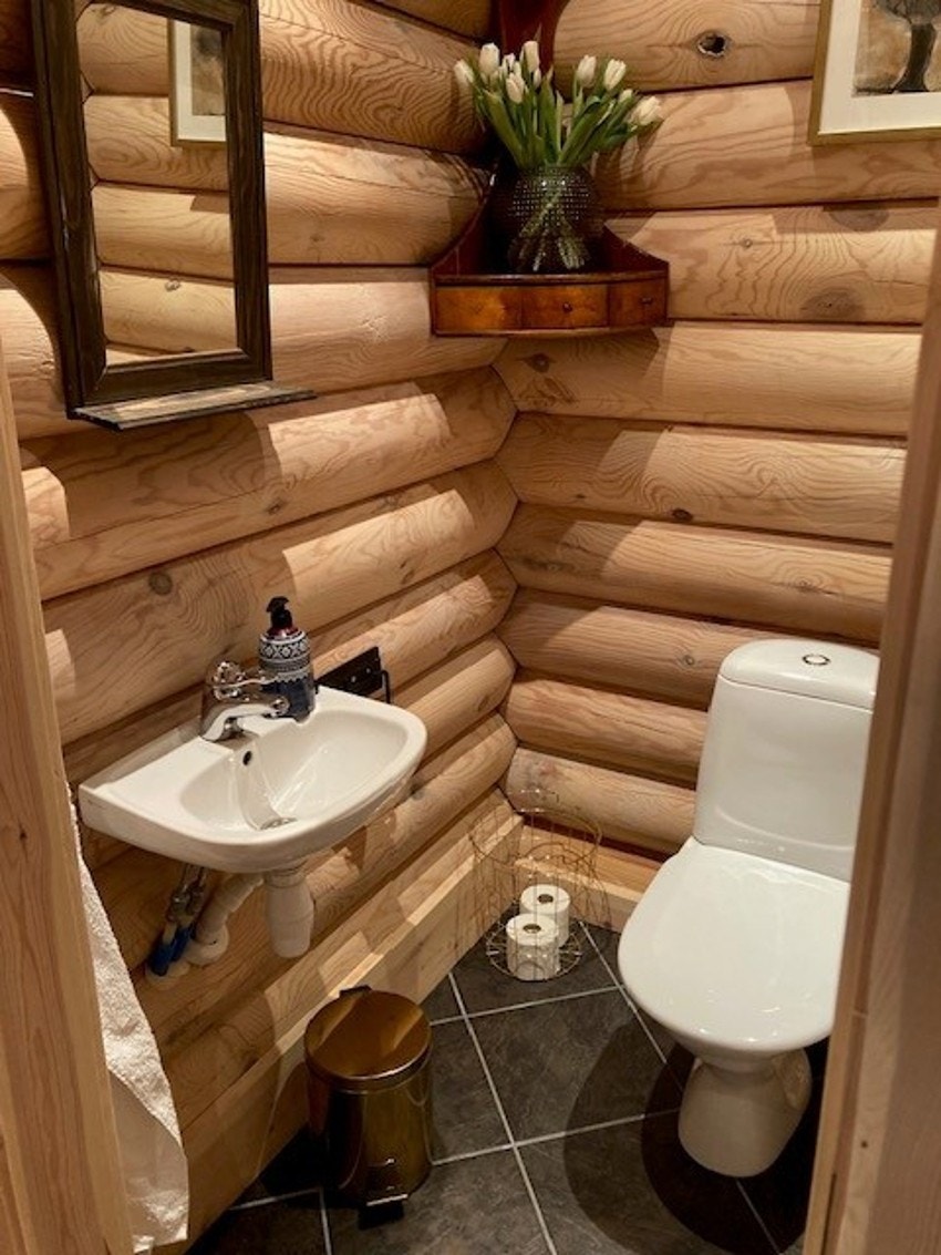 Flislagt toalettrom innredet med gulvstående toalett, vegghengt servant samt speil på vegg over servant. Galleribilde