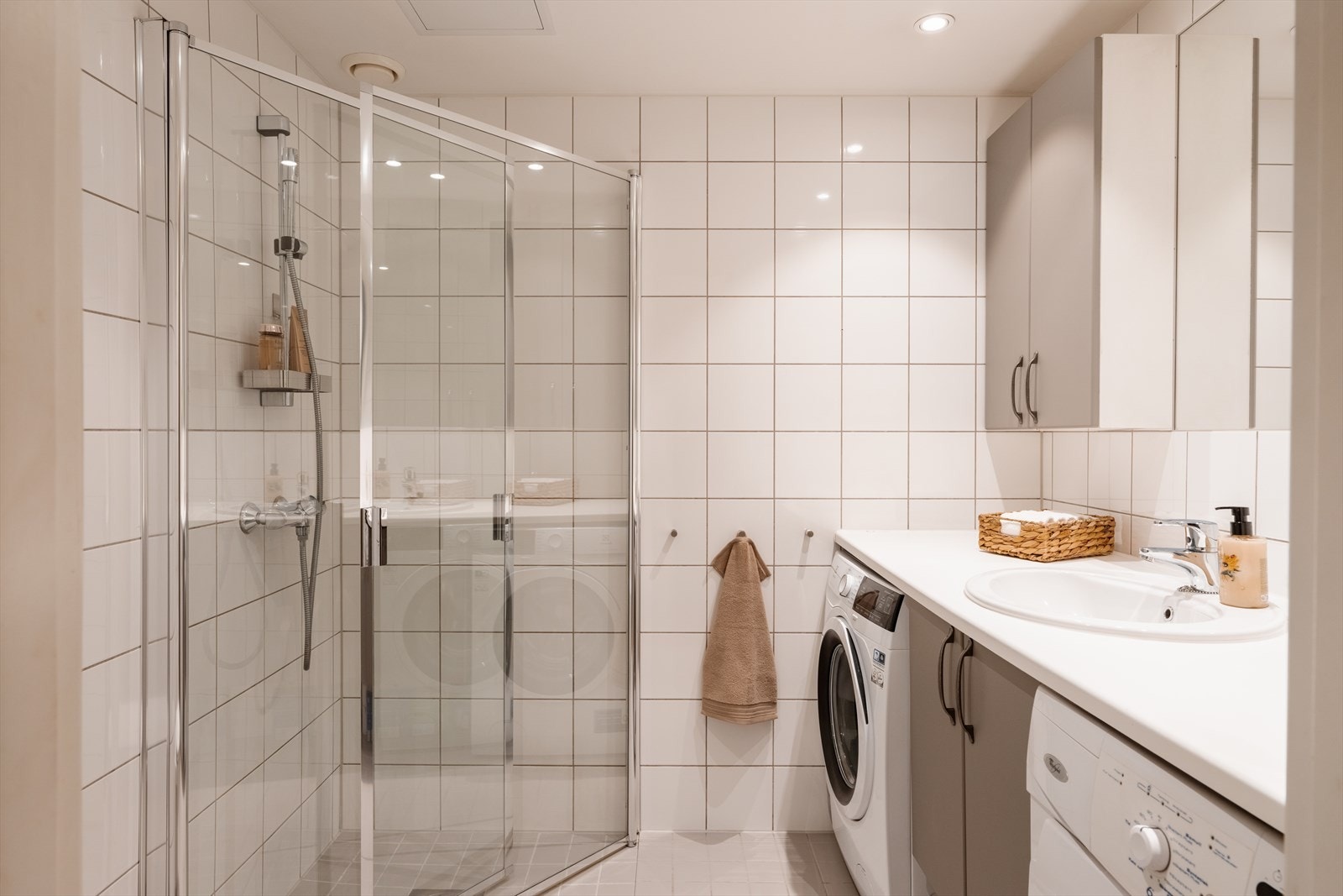 Helfliset bad med dusjhjørne med innfellbare glassdører og opplegg for vaskemaskin. Galleribilde