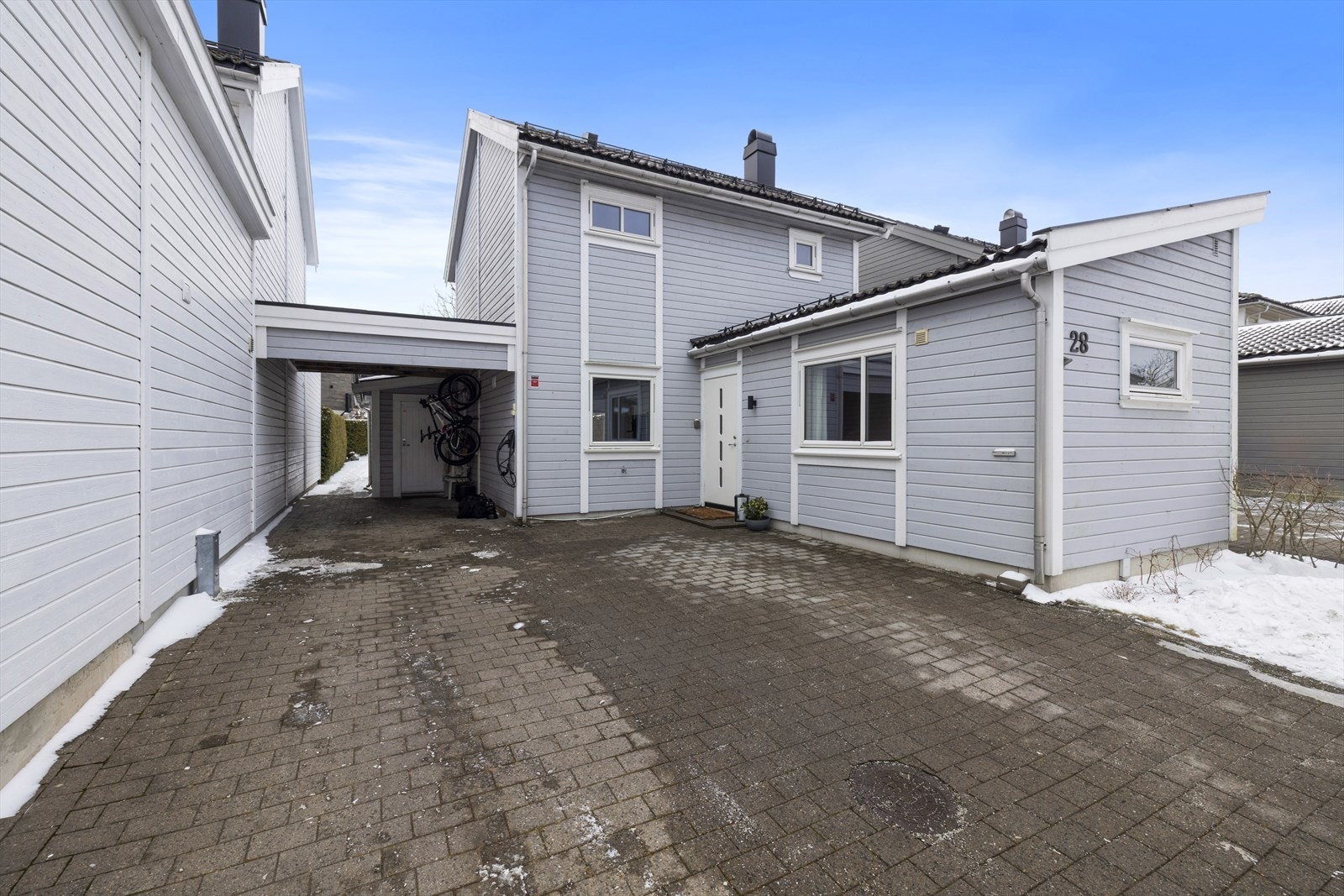 Boligen har en praktisk carport med montert elbillader. I tillegg er det god plass til gjesteparkering på den stenlagte gårdsplassen. Galleribilde