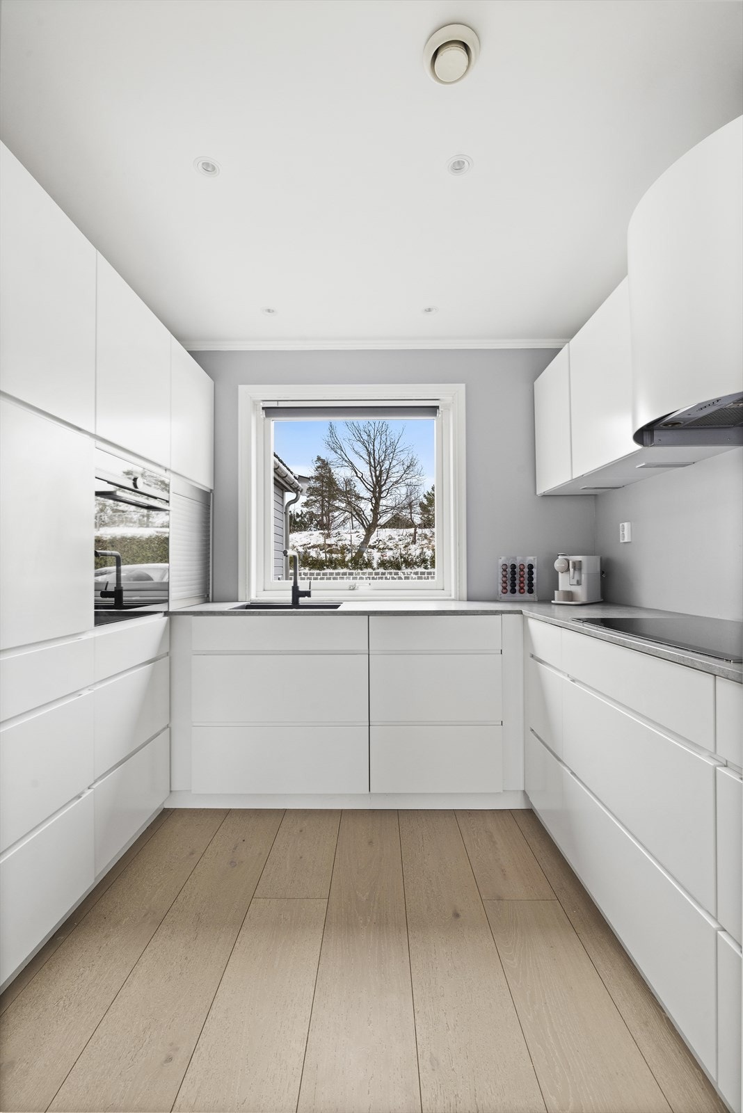 Kjøkkenet er holdt i en minimalistisk stil med hvite, slette fronter og integrerte hvitevarer. Vindu i enden gir godt med naturlig lysinnslipp. Galleribilde