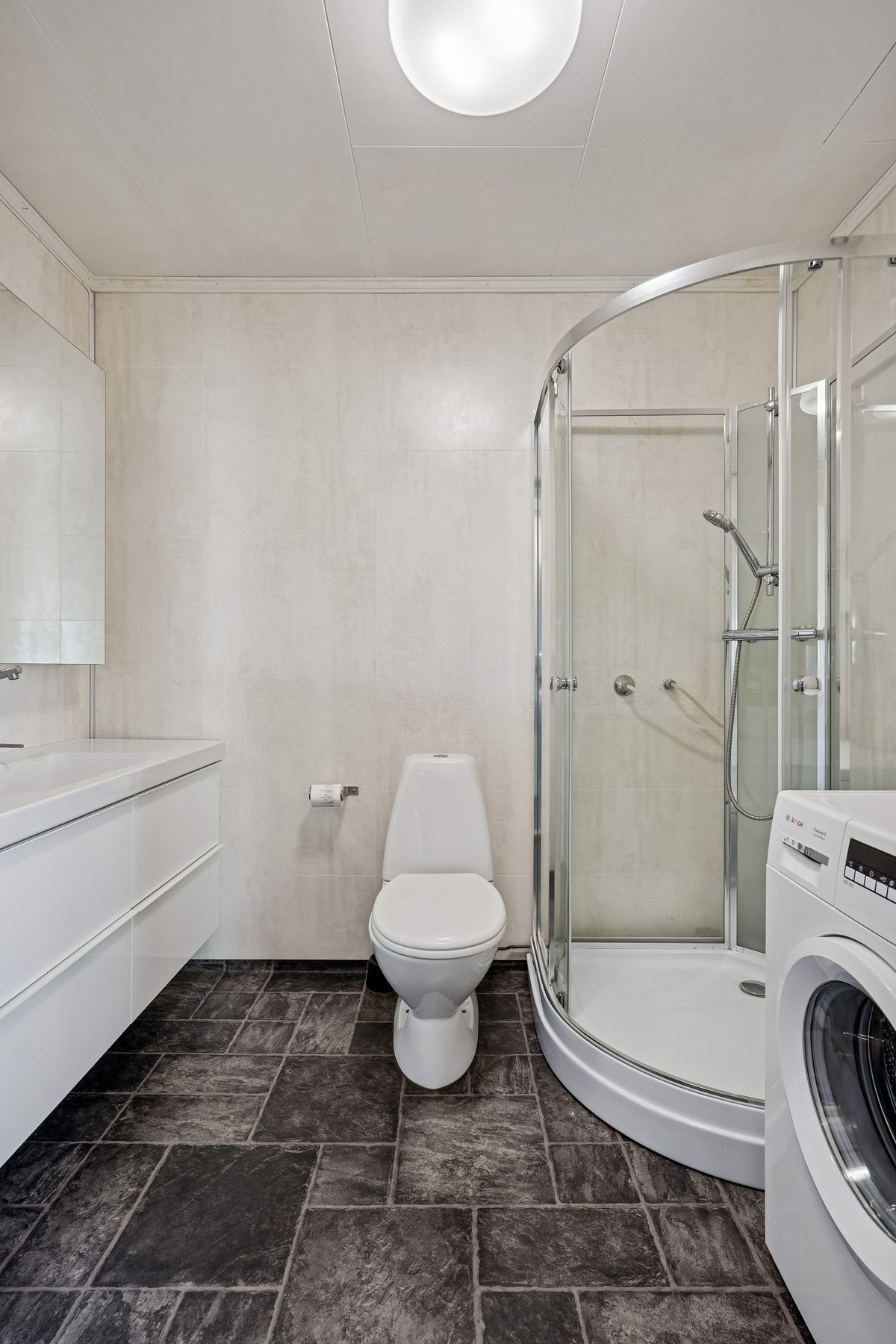 Badet har innredning med nedfelt servant, toalett, dusjkabinett og opplegg for vaskemaskin Galleribilde