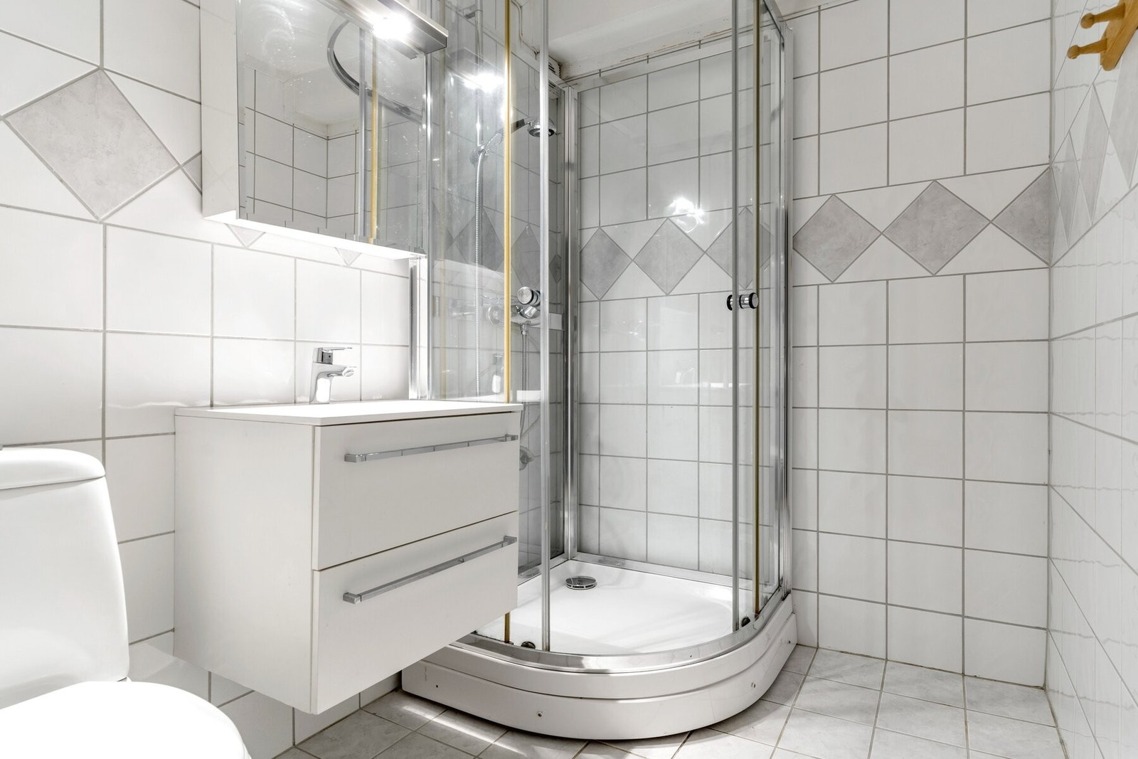 Flislagt bad innredet med dusjkabinett, toalett og servantskap med skuffer. Galleribilde