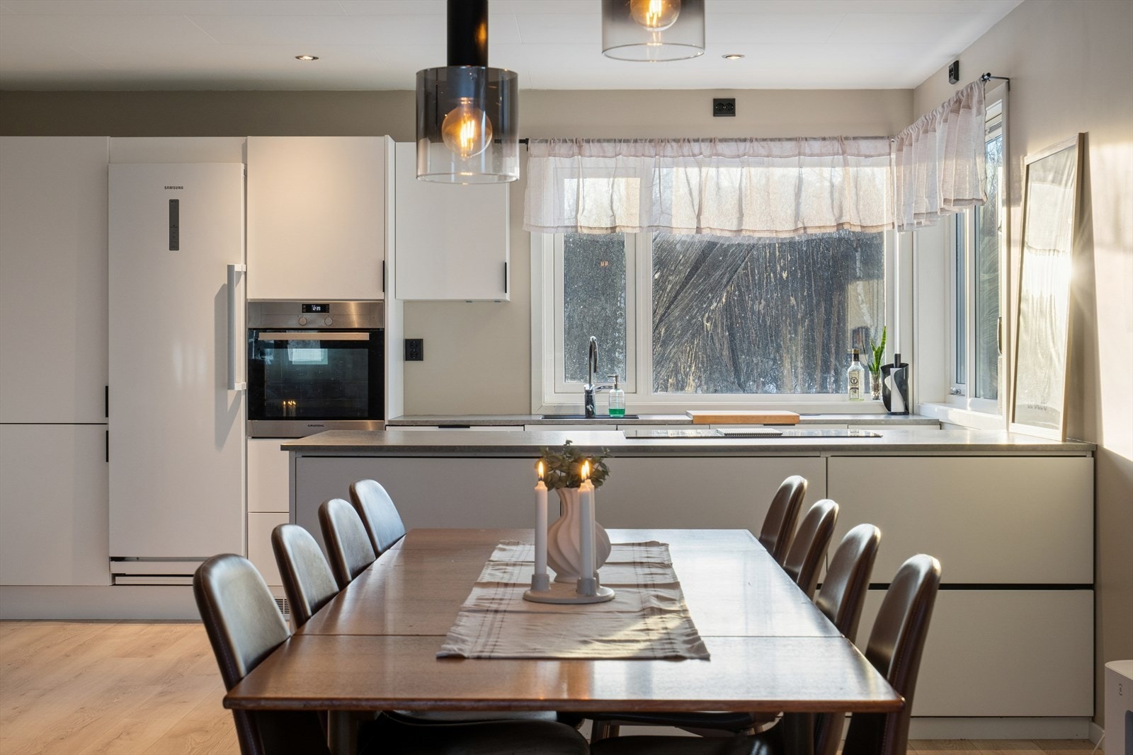 Kjøkkenet er innredet med hvite, glatte fronter og har rikelig med skap- og benkeplass, inkludert en romslig kjøkkenøy mot stuedelen Galleribilde