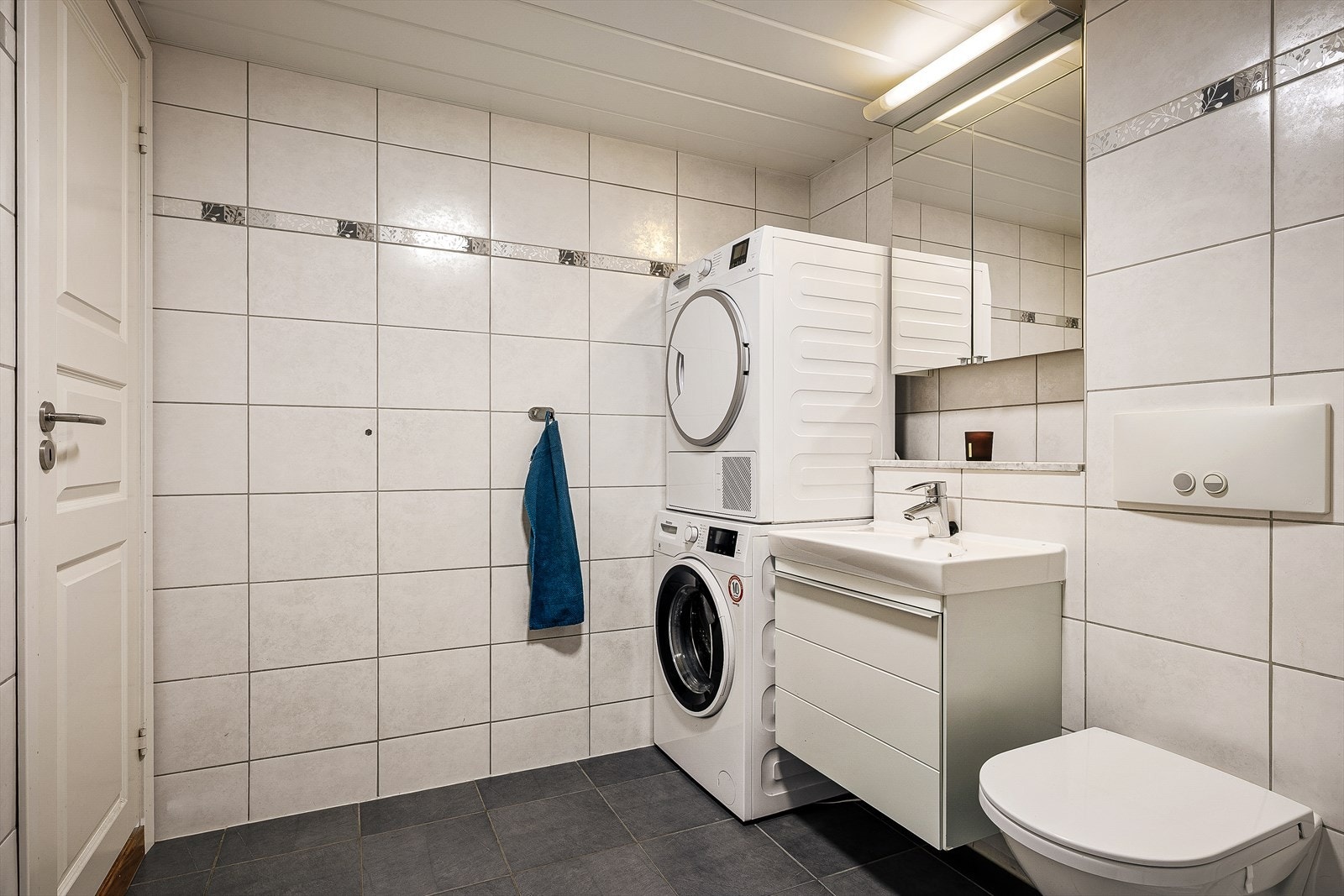 Helfliset bad innredet med servant, møbler, veggmontert toalett og opplegg for vaskemaskin. Galleribilde