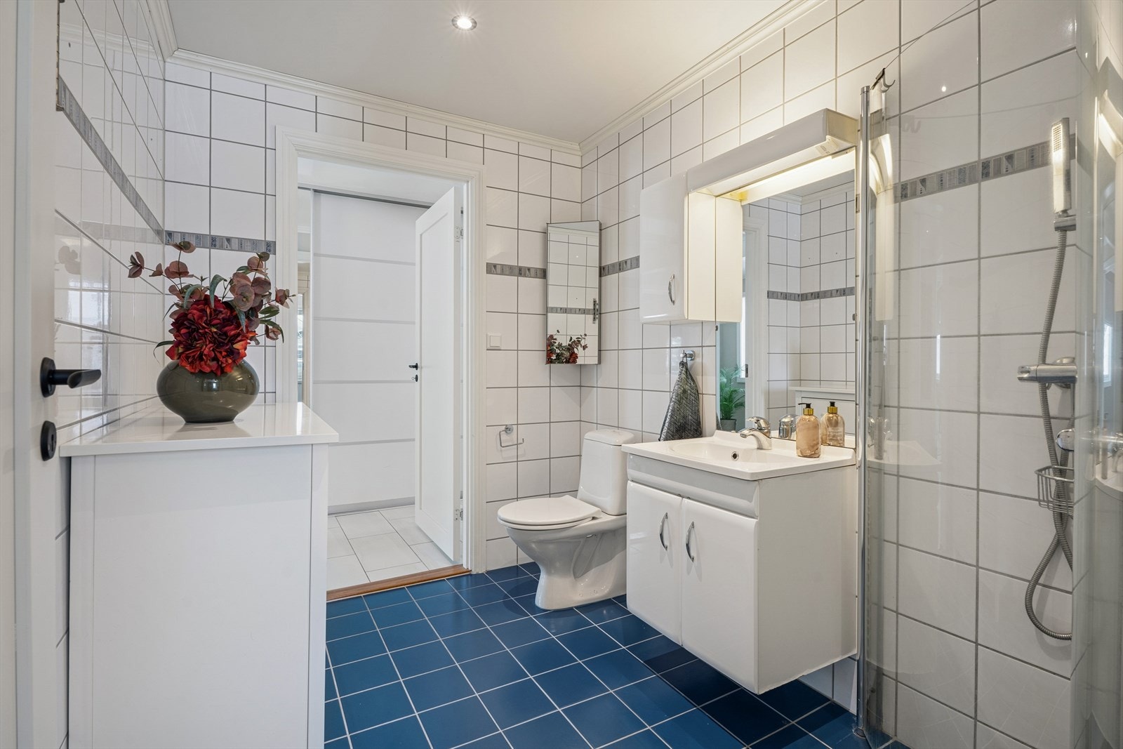 Rommet er utstyrt med en innredning med nedfelt servant, et gulvstående toalett og et dusjhjørne med vegger. Galleribilde