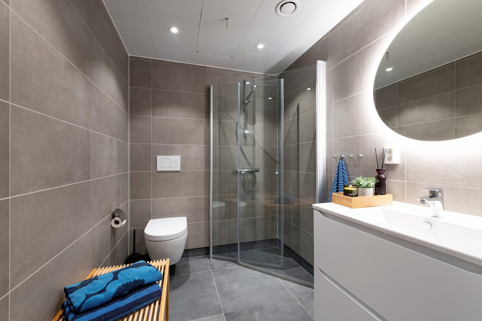 Flislagt bad nr 2 med gulvvarme, dusjhjørne, vegghengt toalett, vegghengt servantinnredning og speil med side lys Galleribilde