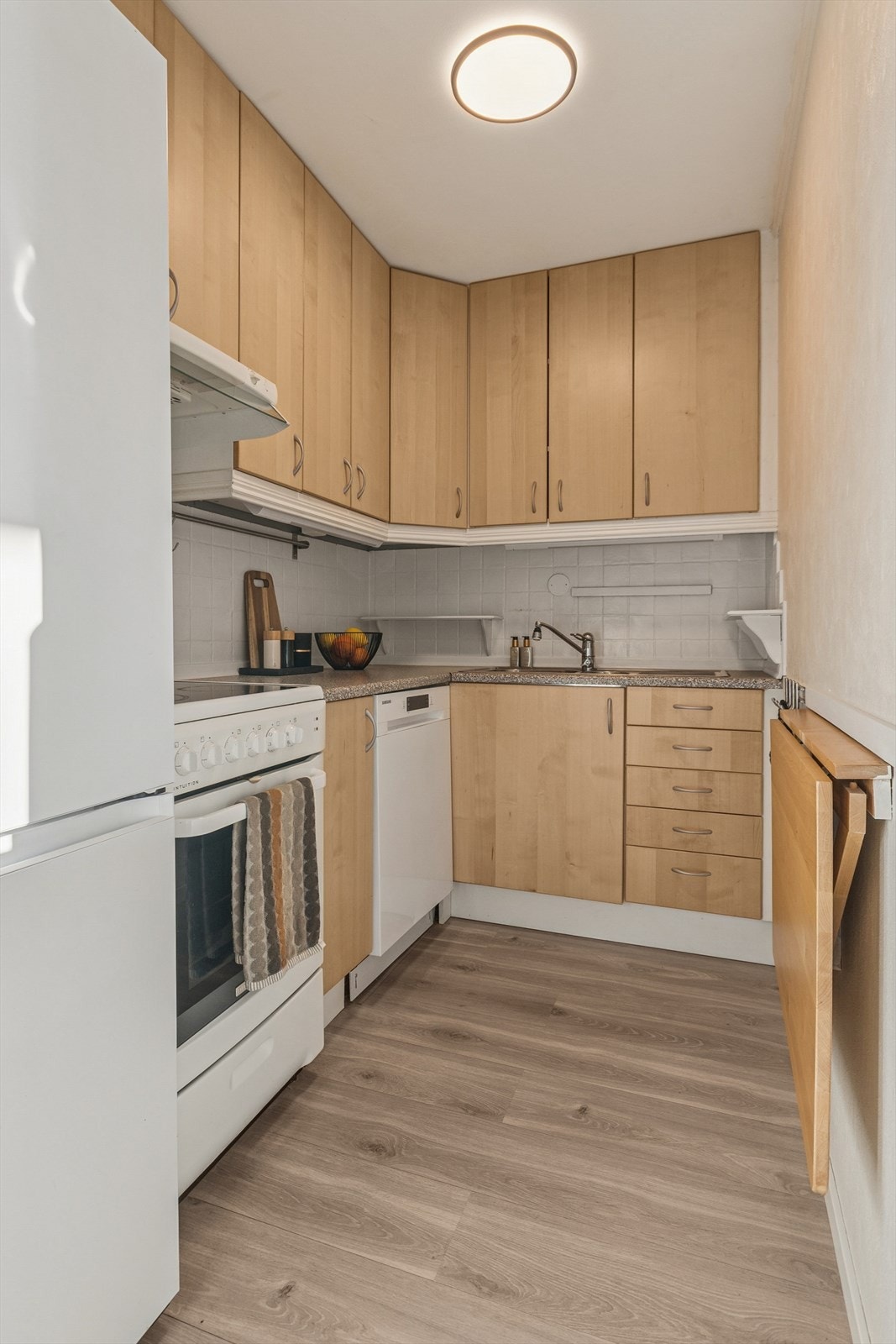 Lyst kjøkken med slette fronter og benkeplate av typen laminat. Galleribilde