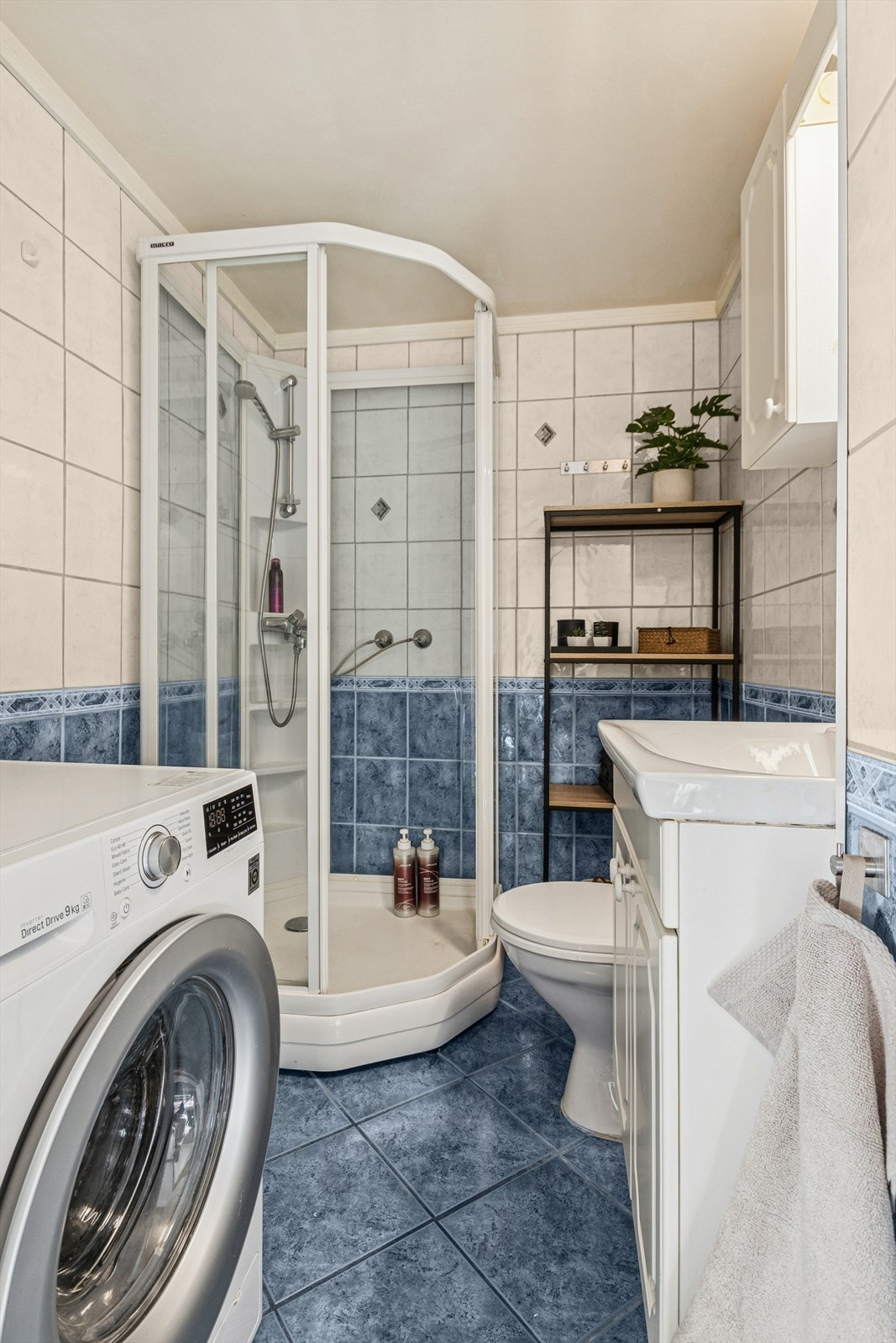 Pent flislagt bad utstyrt med dusjkabinett, gulvstående toalett og opplegg for vaskemaskin. Galleribilde