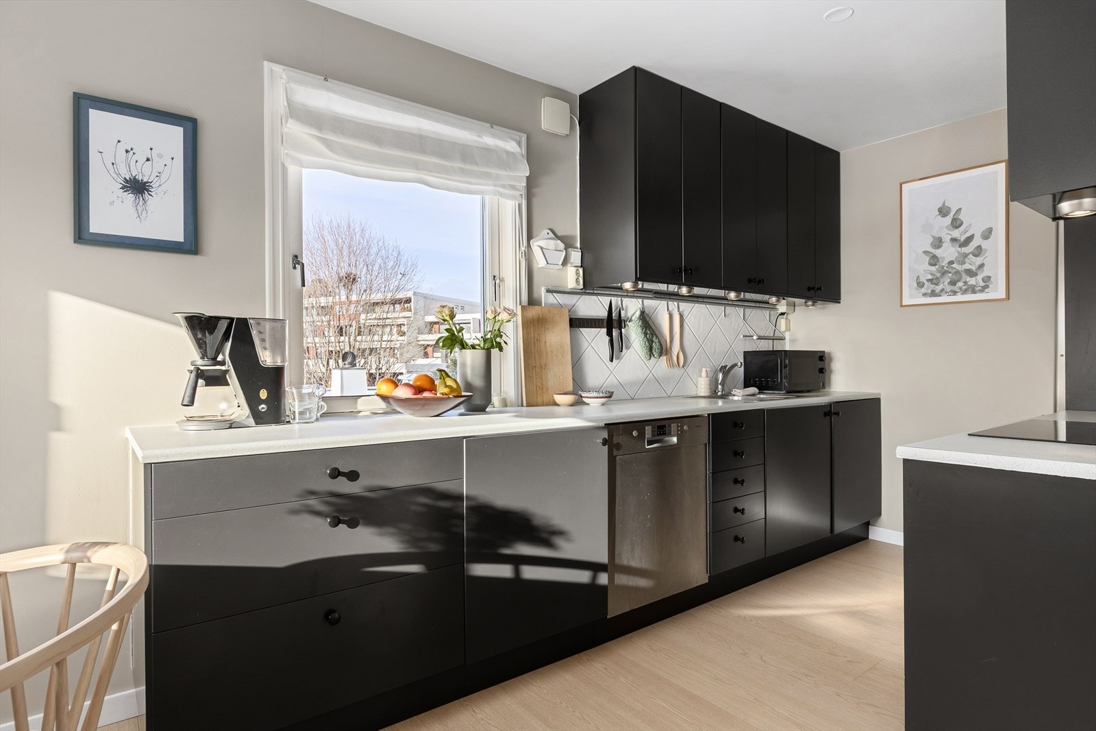 Kjøkkeninnredning har glatte fronter, fliser på vegg over benkeskap og laminat benkeplate med nedfelt kum i rustfritt stål. Galleribilde