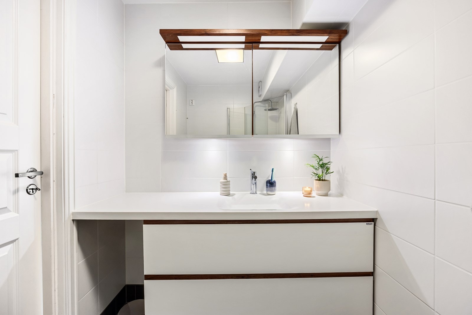 Baderomsinnredningen bestående av benkeskap med glatte fronter og veggskap med speil fronter. Servant, dusj, opplegg for vaskemaskin og elektrisk avtrekksvifte. Det er gulvvarme på både bad og toalett. Galleribilde