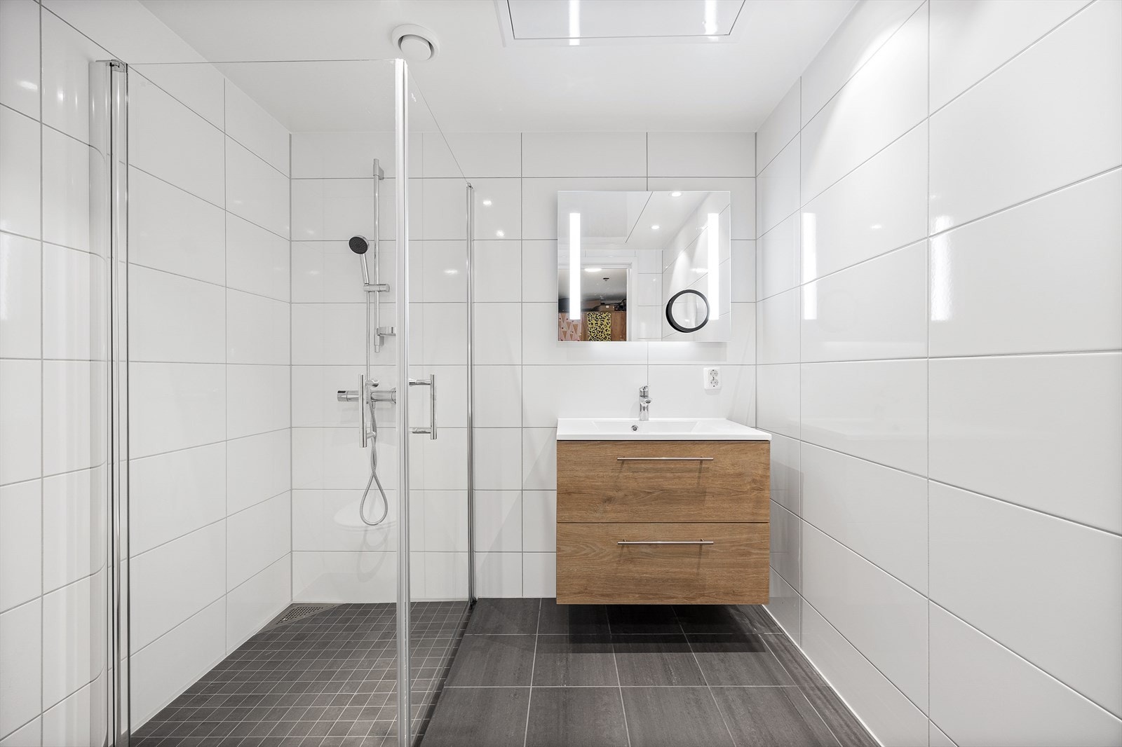 Badet er innredet med servant, vegghengt toalett, speil med lys og dusjhjørne Galleribilde