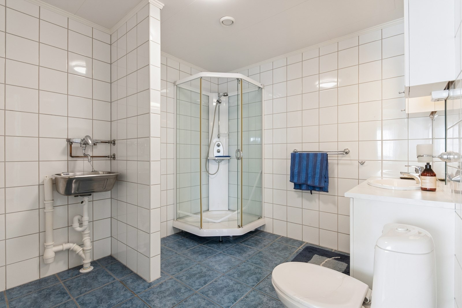 Lyst og pent bad/vaskerom utstyrt med dusjkabinett, gulvstående toalett og opplegg for vaskemaskin. Galleribilde