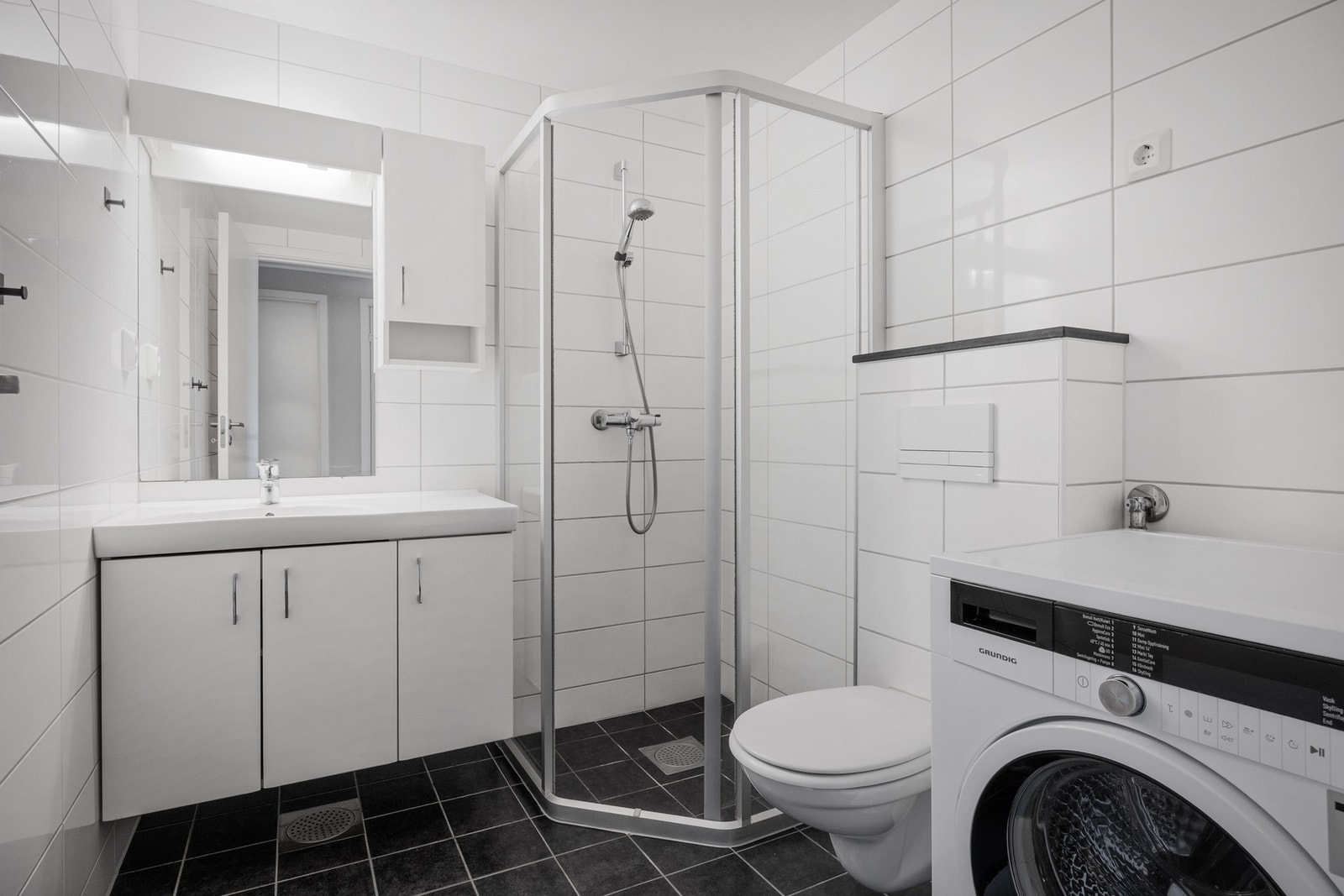 Badet er innredet med servant, dusjhjørne, toalett og opplegg for vaskemaskin Galleribilde