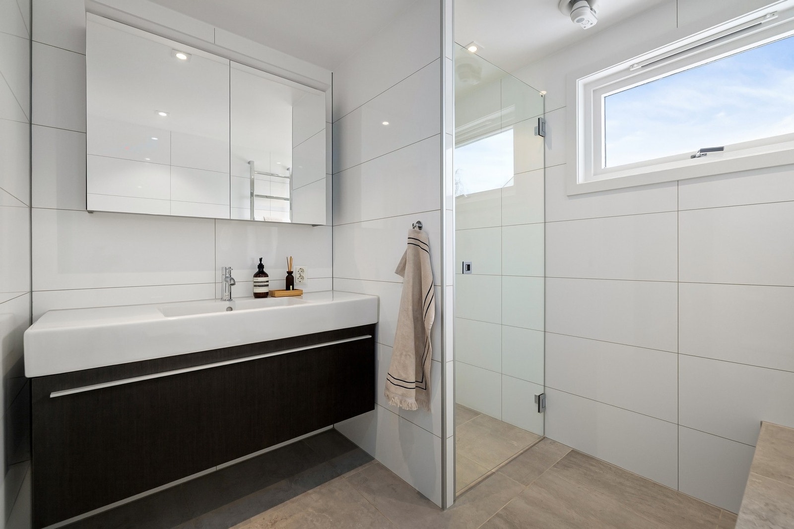 Badet er utstyrt med varmekabler, avtrekk, speilskap med belysning, downlights, servant med innredning, dusjhjørne med innfellbare glassdører og vegghengt toalett. Galleribilde