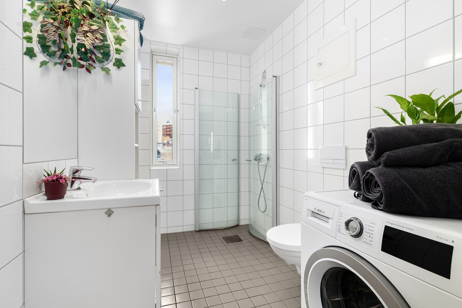 Leiligheten har et lyst og moderne baderom fra byggeåret 2011. I hjørnet er det plass og opplegg for vaskemaskin og tørketrommel over om ønskelig. Galleribilde