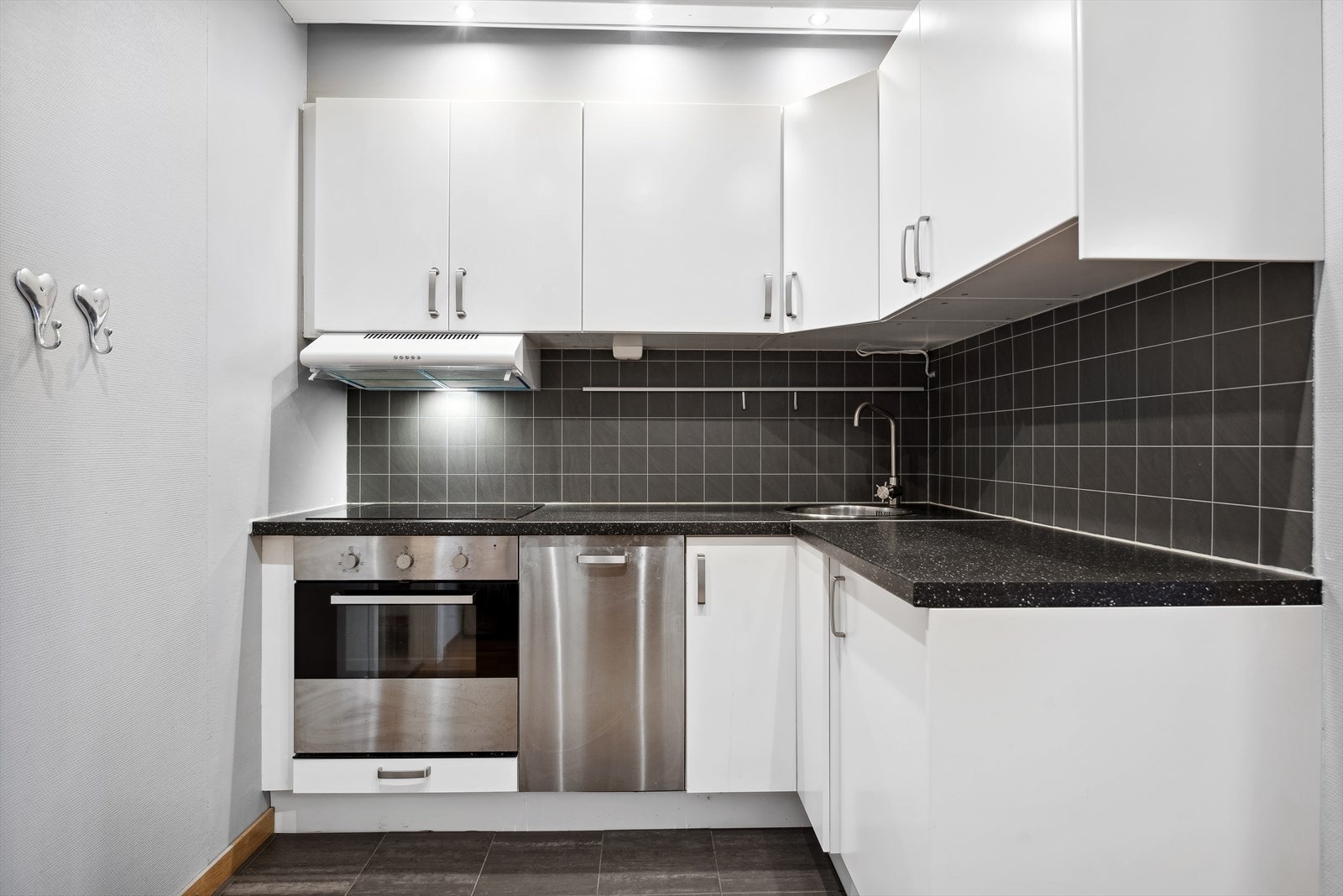 Kjøkkeninnredningen har hvite glatte fronter, laminat benkeplate, nedfelt oppvaskkum, flislignende plate over benk og ventilator. Galleribilde