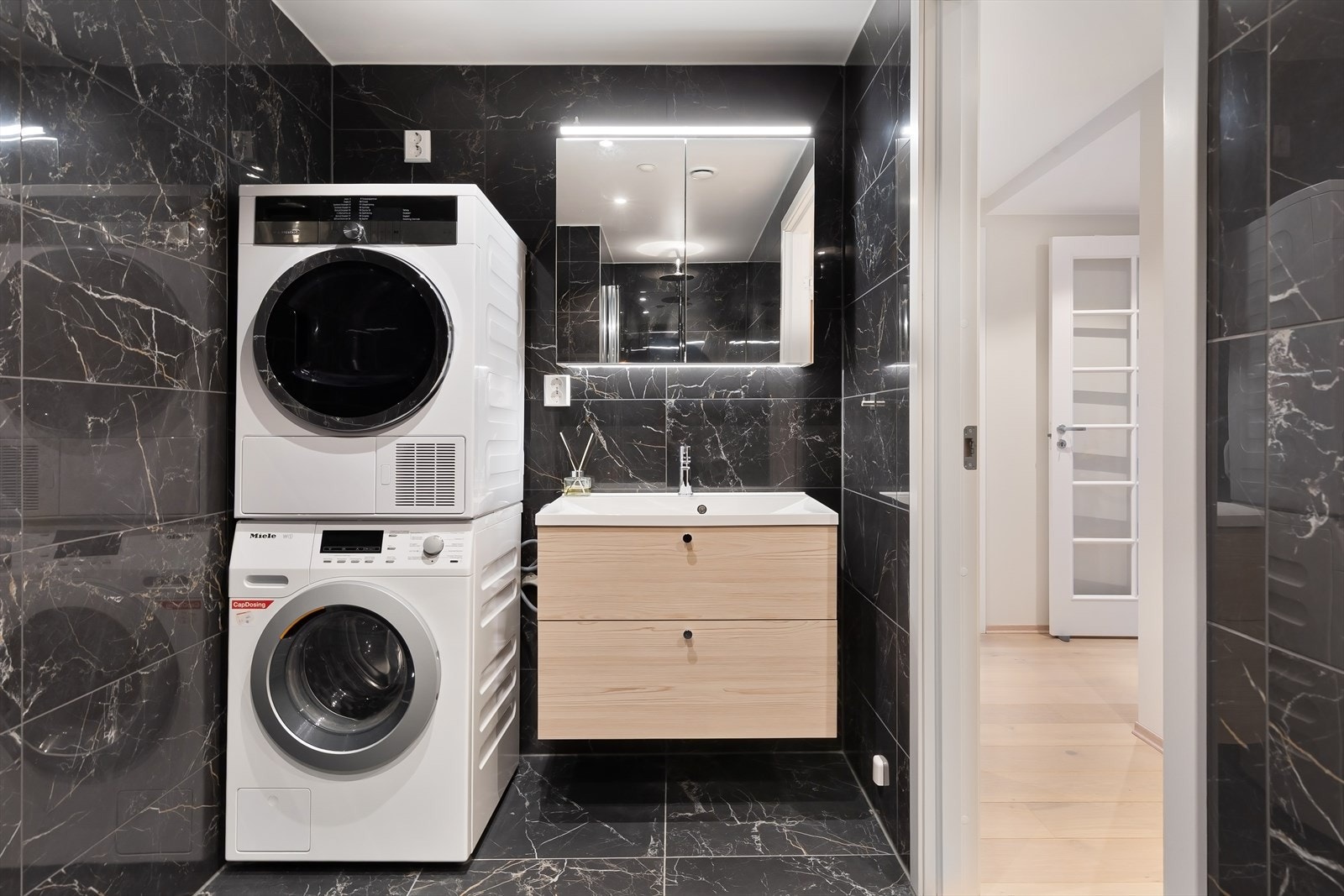 Badet har innredning med nedfelt servant, veggmontert toalett, svingbar dusjvegg i glass samt opplegg for vaskemaskin. Galleribilde