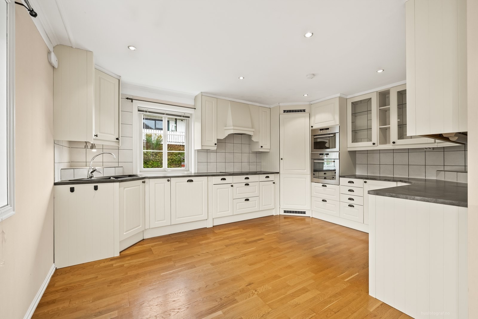 Tiltalende kjøkken med hvit profilert kjøkkeninnredning, god spiseplass og kjølehjørne. Galleribilde